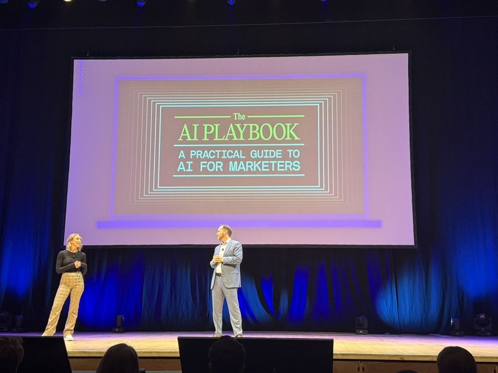 Two presenters on stage with a screen showing The AI Playbook for marketers