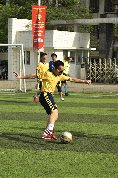 Man wearing yellow jersey kicking soccer ball on green field during match