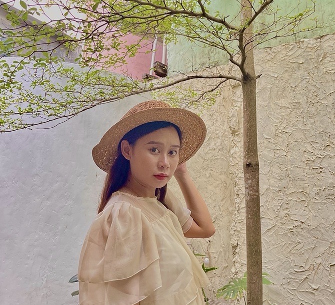 Young woman wearing a straw hat and beige dress under tree branches