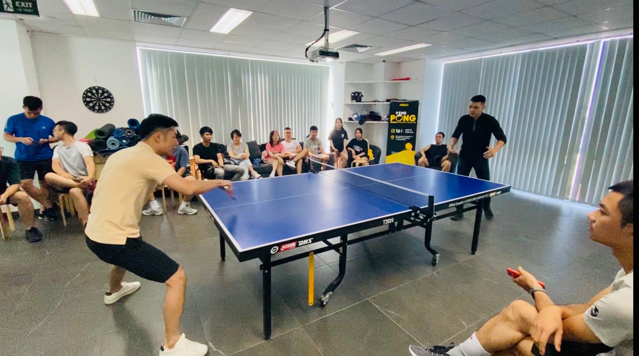 Office ping pong tournament with colleagues playing and others watching closely