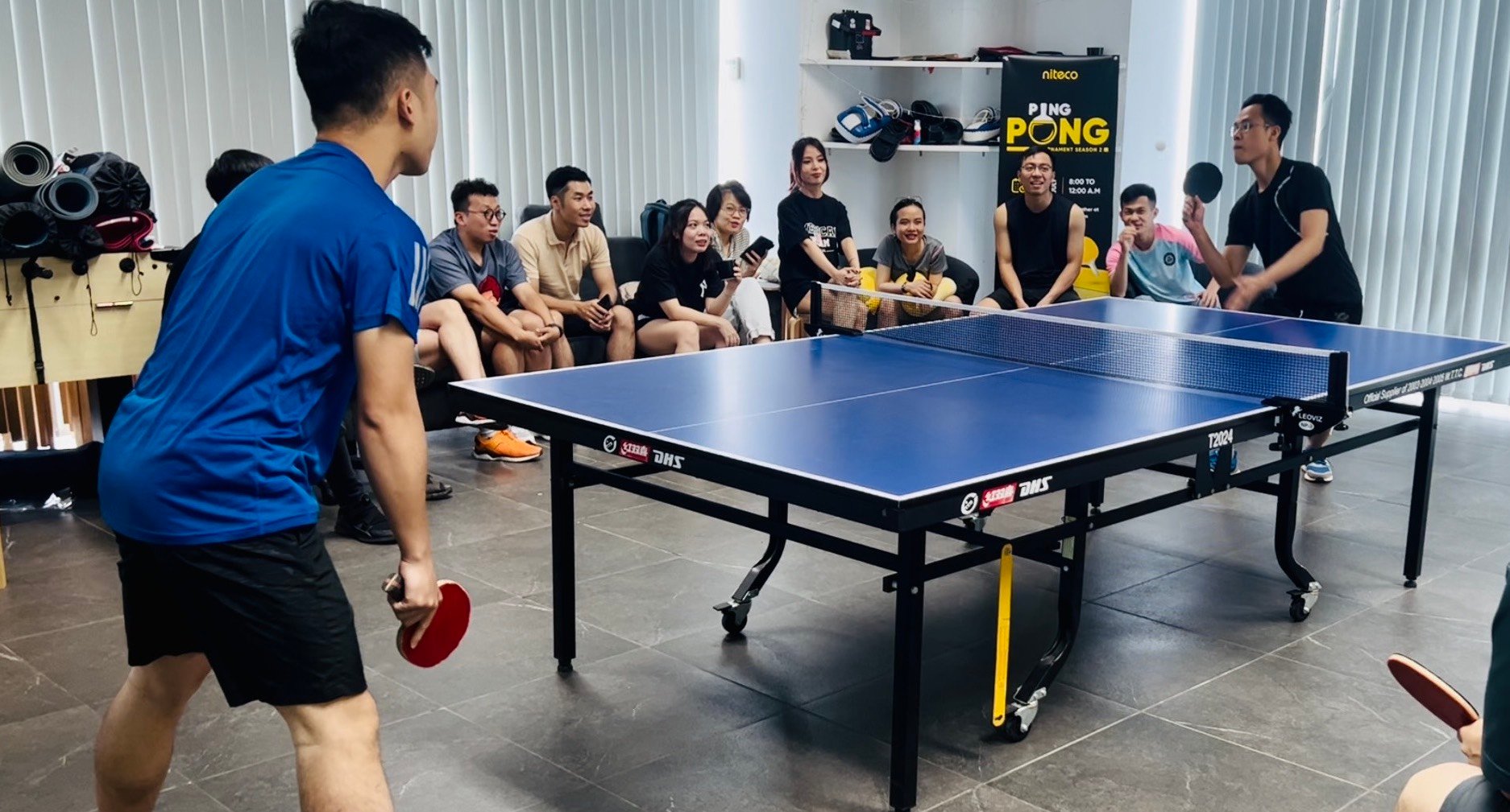 Group playing competitive ping pong with spectators watching indoors