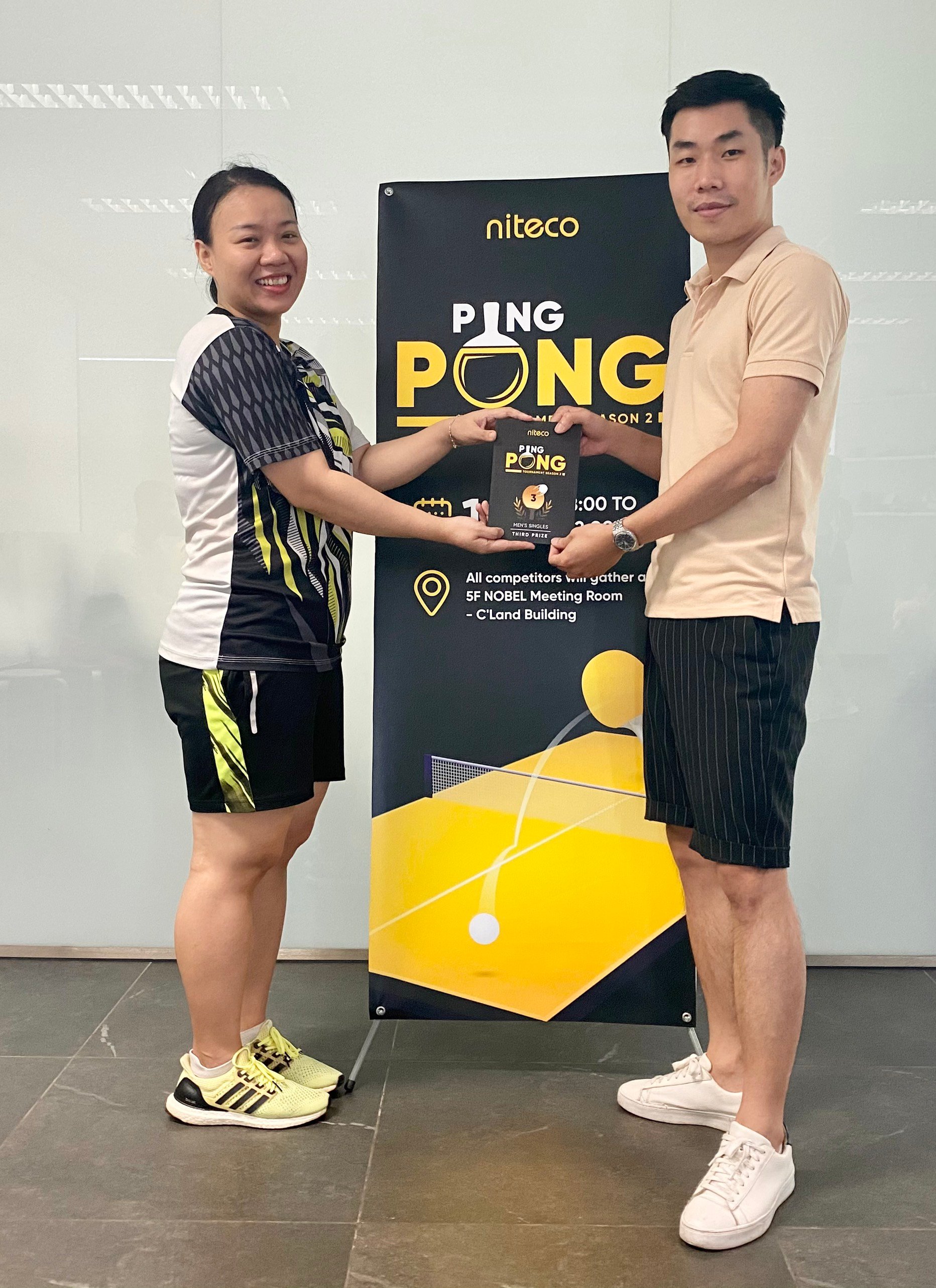 Two people holding third prize award at Niteco Ping Pong tournament banner