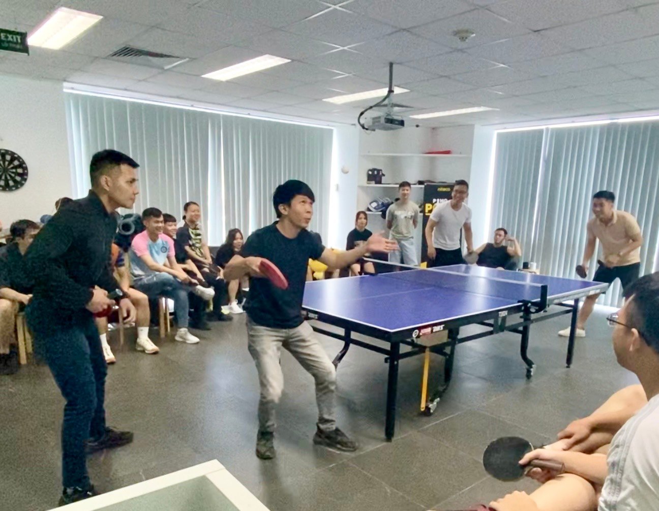Office table tennis match with employees playing and spectators cheering indoors