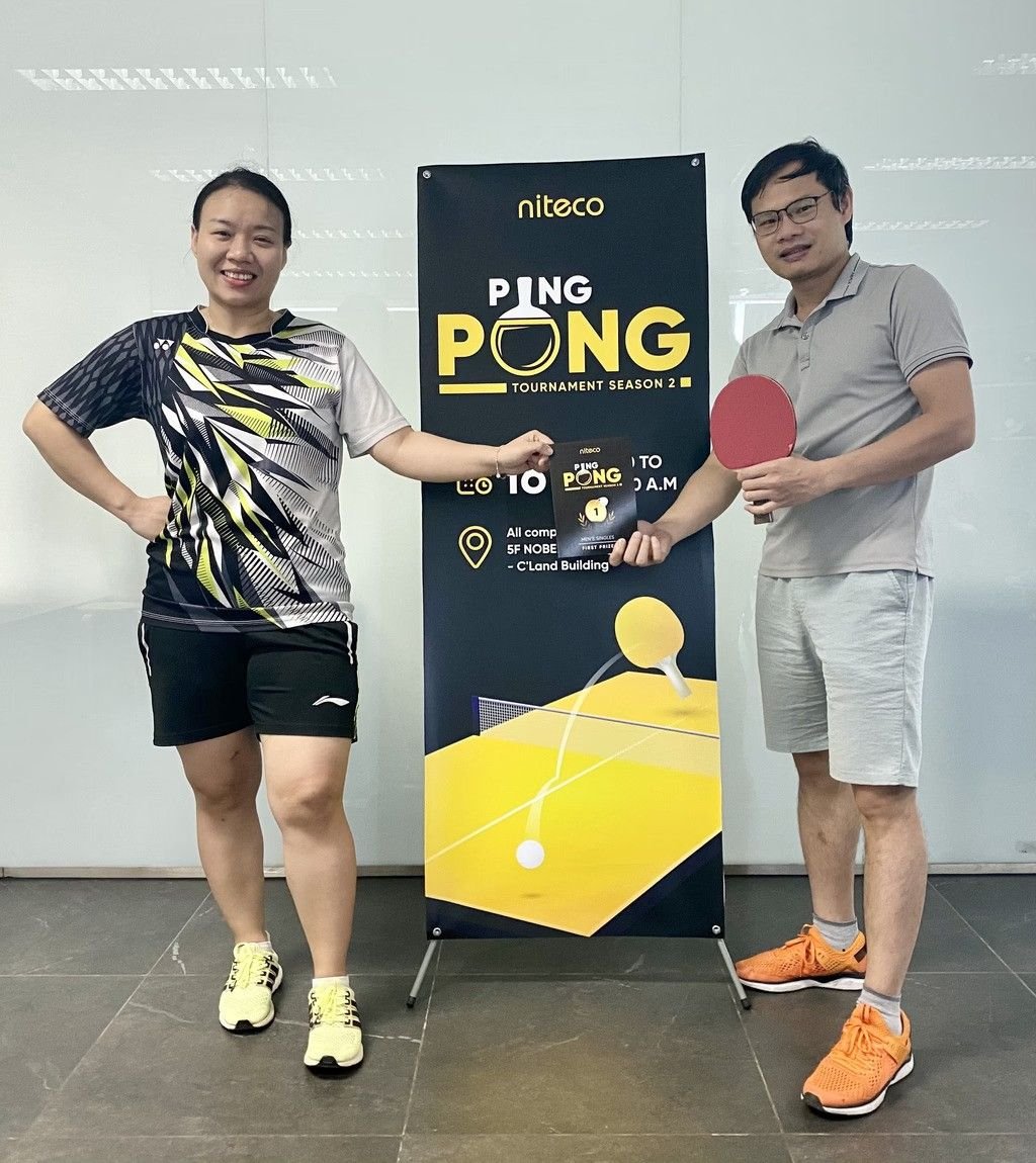 Two players holding a ping pong paddle and award at Niteco Ping Pong Tournament banner