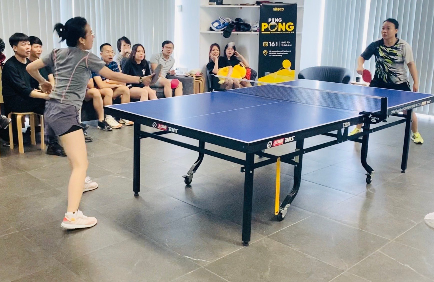 Two women competing in a ping pong tournament with spectators watching closely