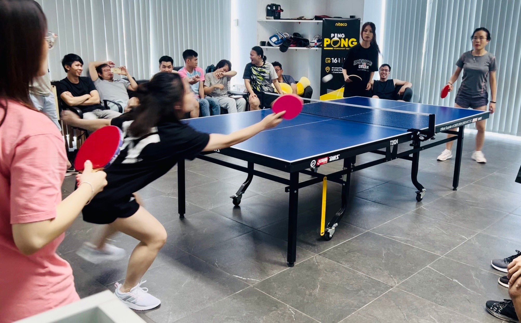 Indoor ping pong tournament with players and audience in casual setting