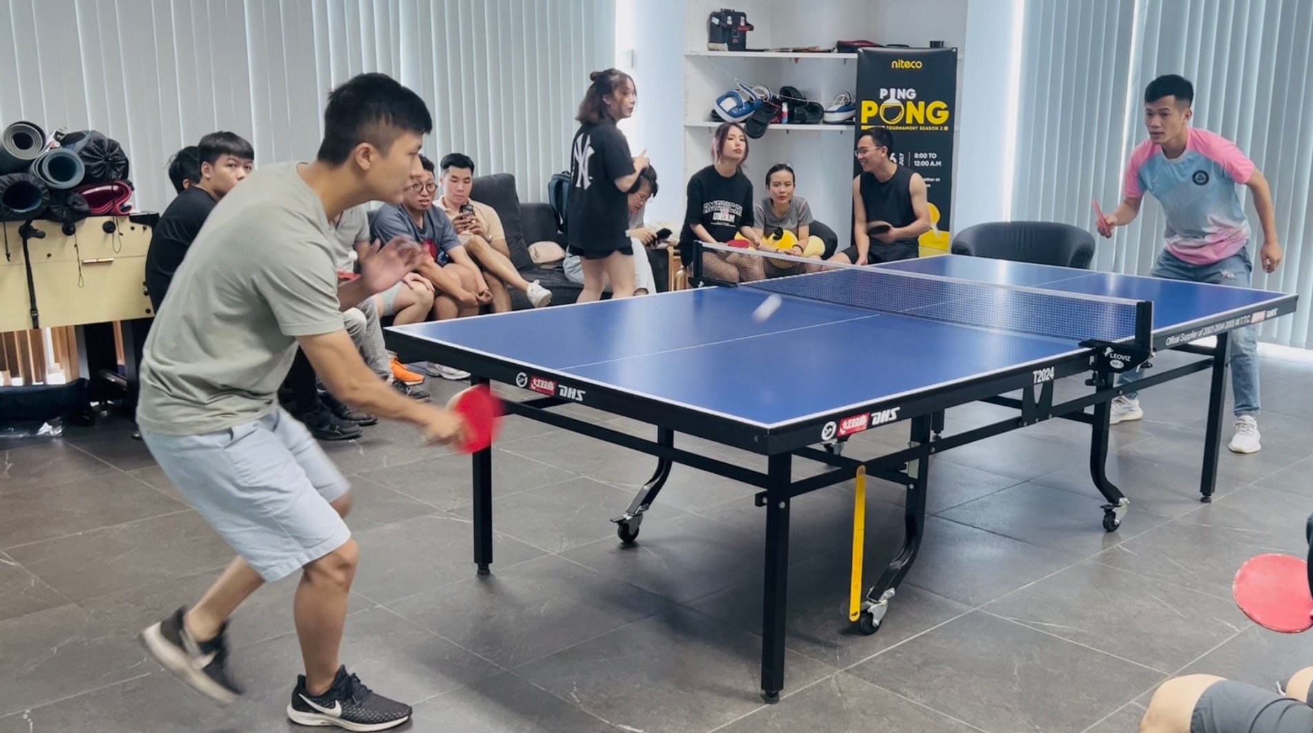 Young men playing ping pong in an indoor tournament with spectators watching