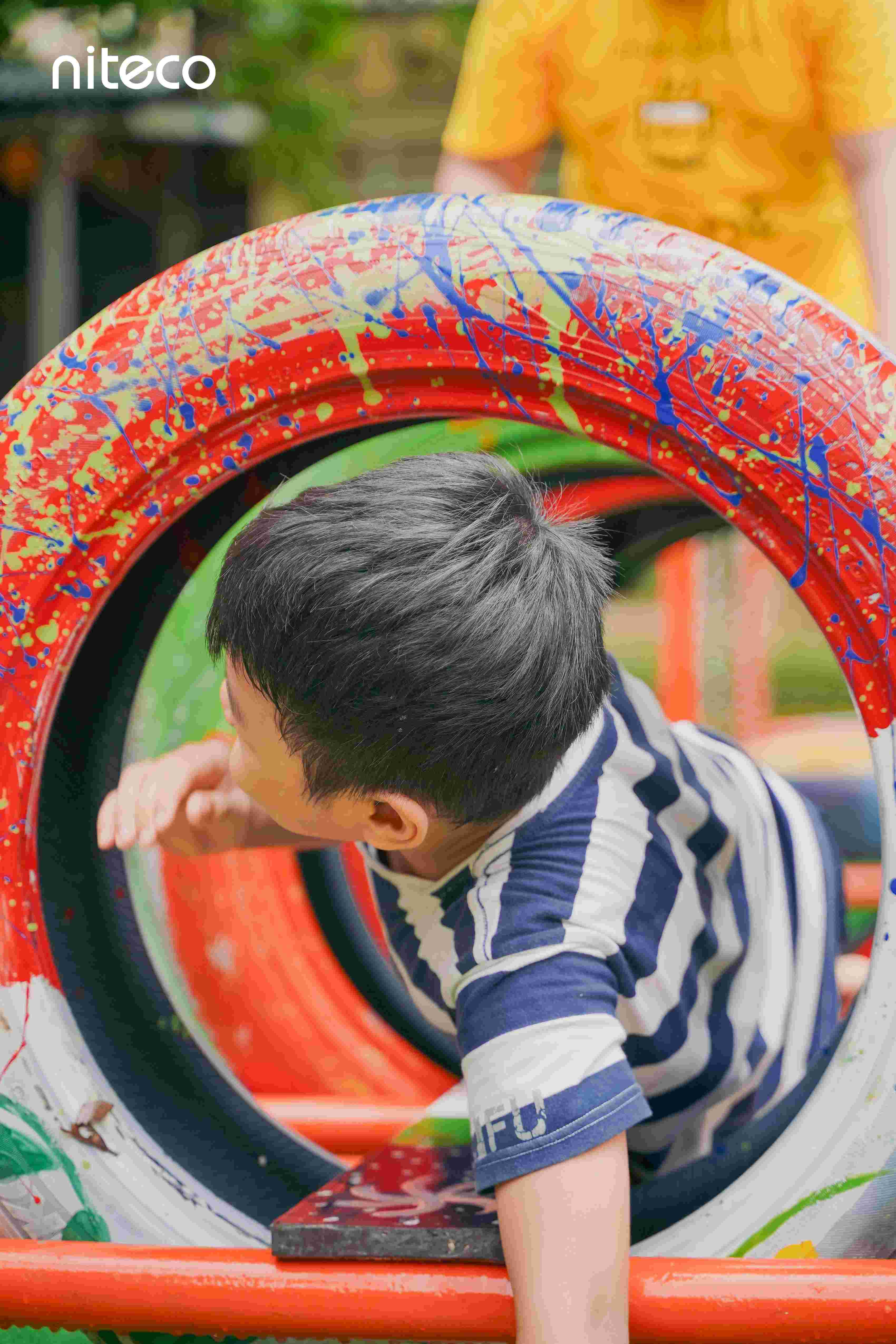 Boy crawling through colorful tire obstacle in outdoor activity by Niteco