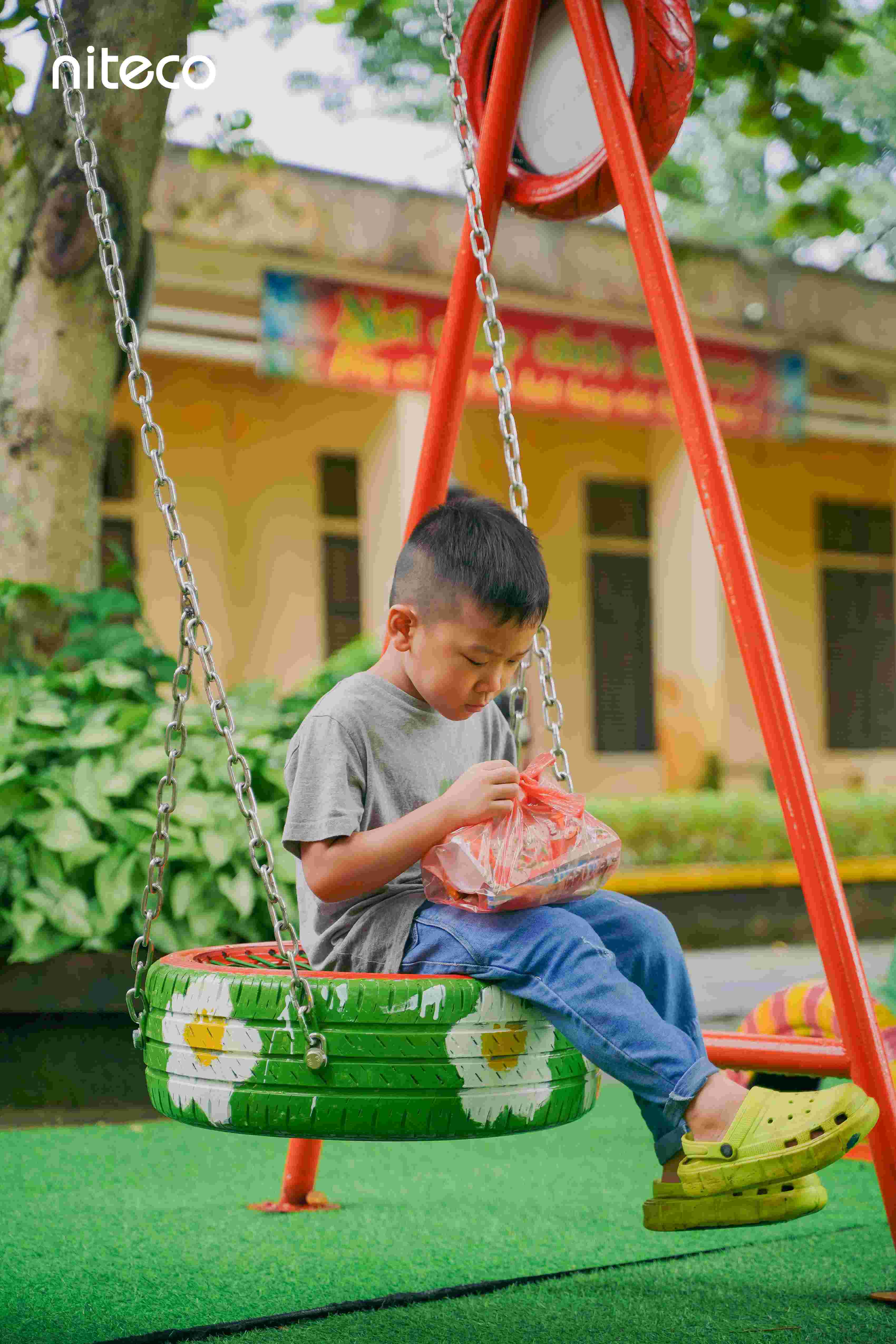 Boy sitting on painted tire swing holding a snack bag in playground