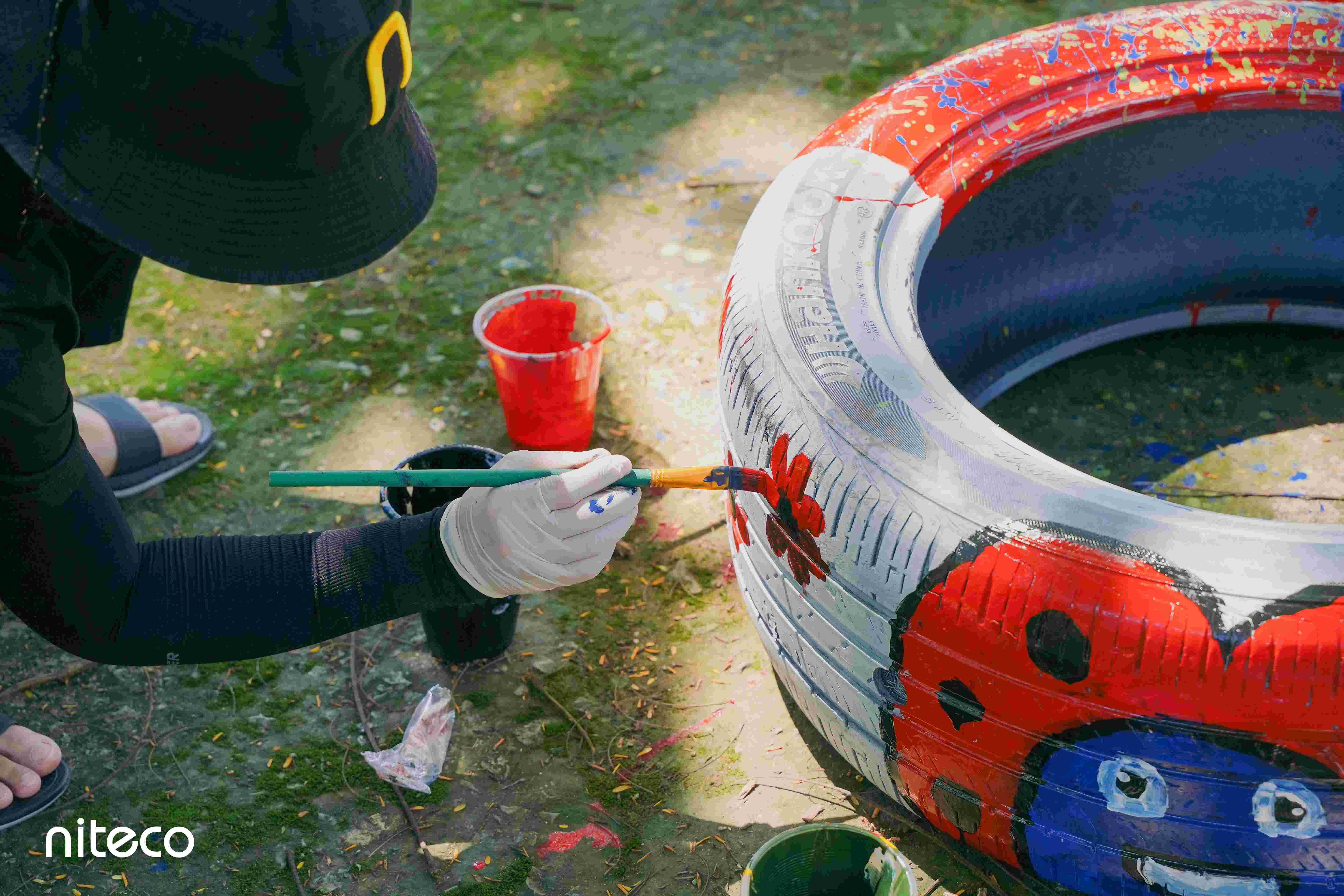 Person painting a red ladybug design on a white tire for outdoor decoration