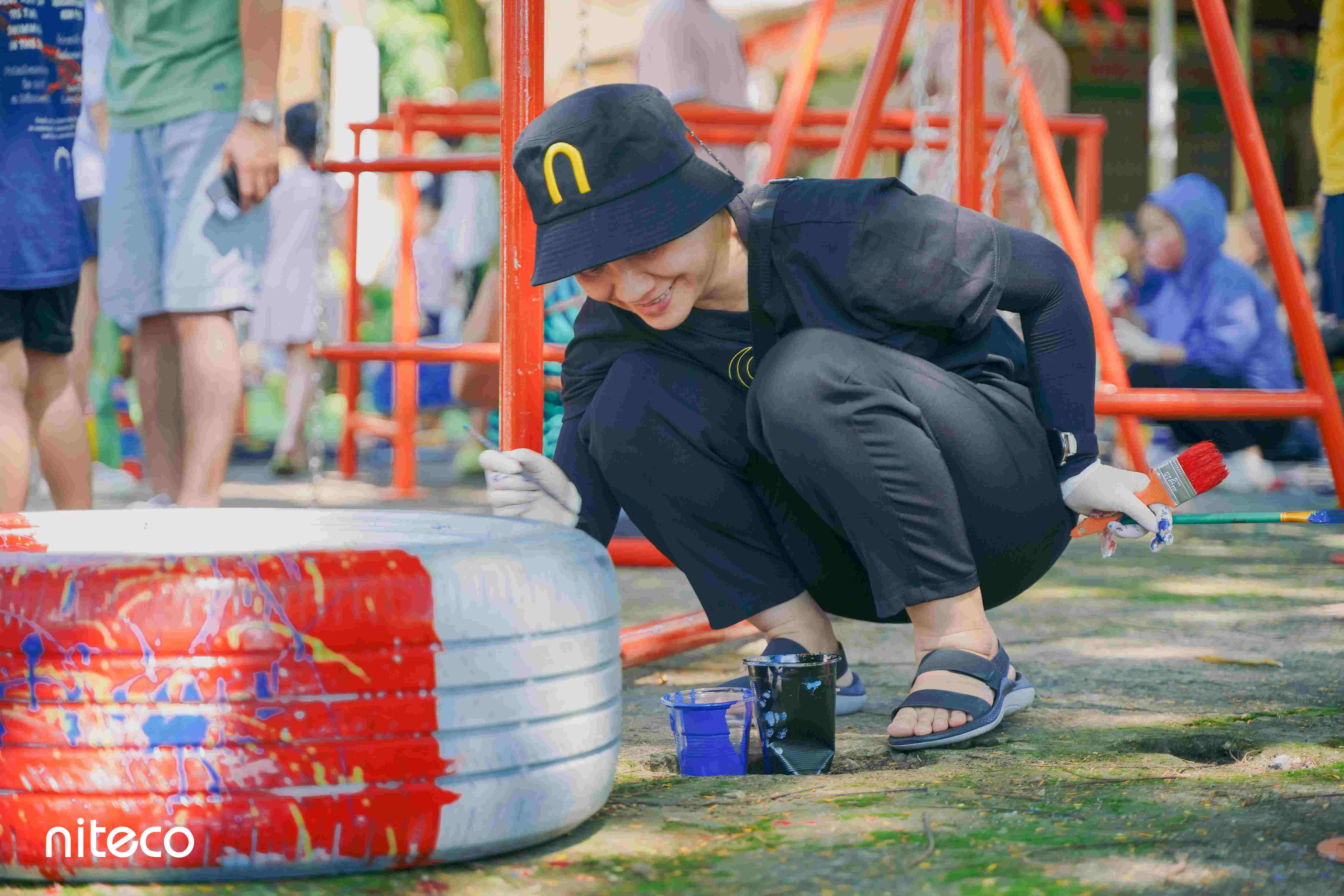 Young volunteer painting playground tire with red and blue paint outdoors