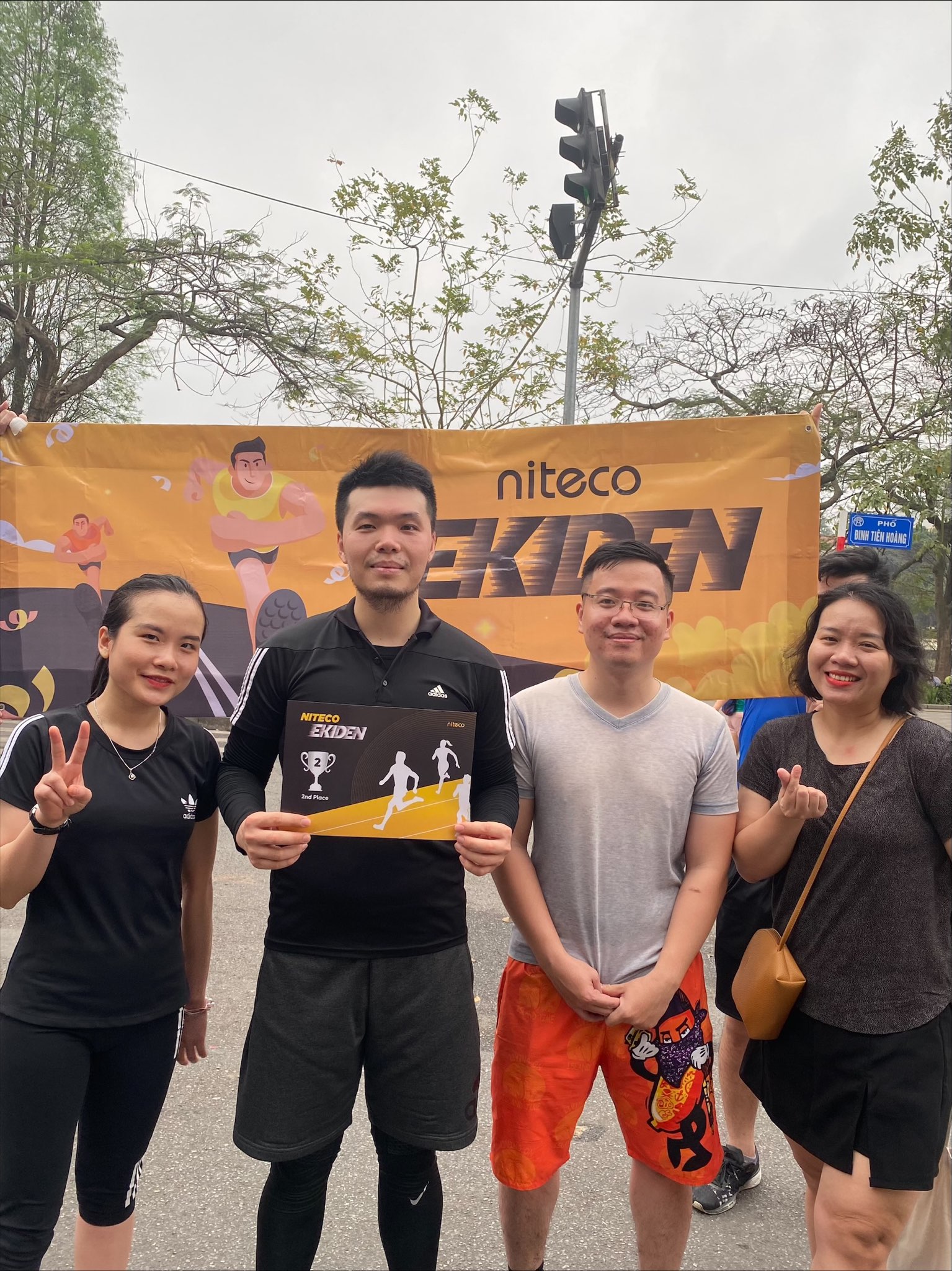 Niteco Ekiden team celebrating 2nd place award outdoors with banner behind