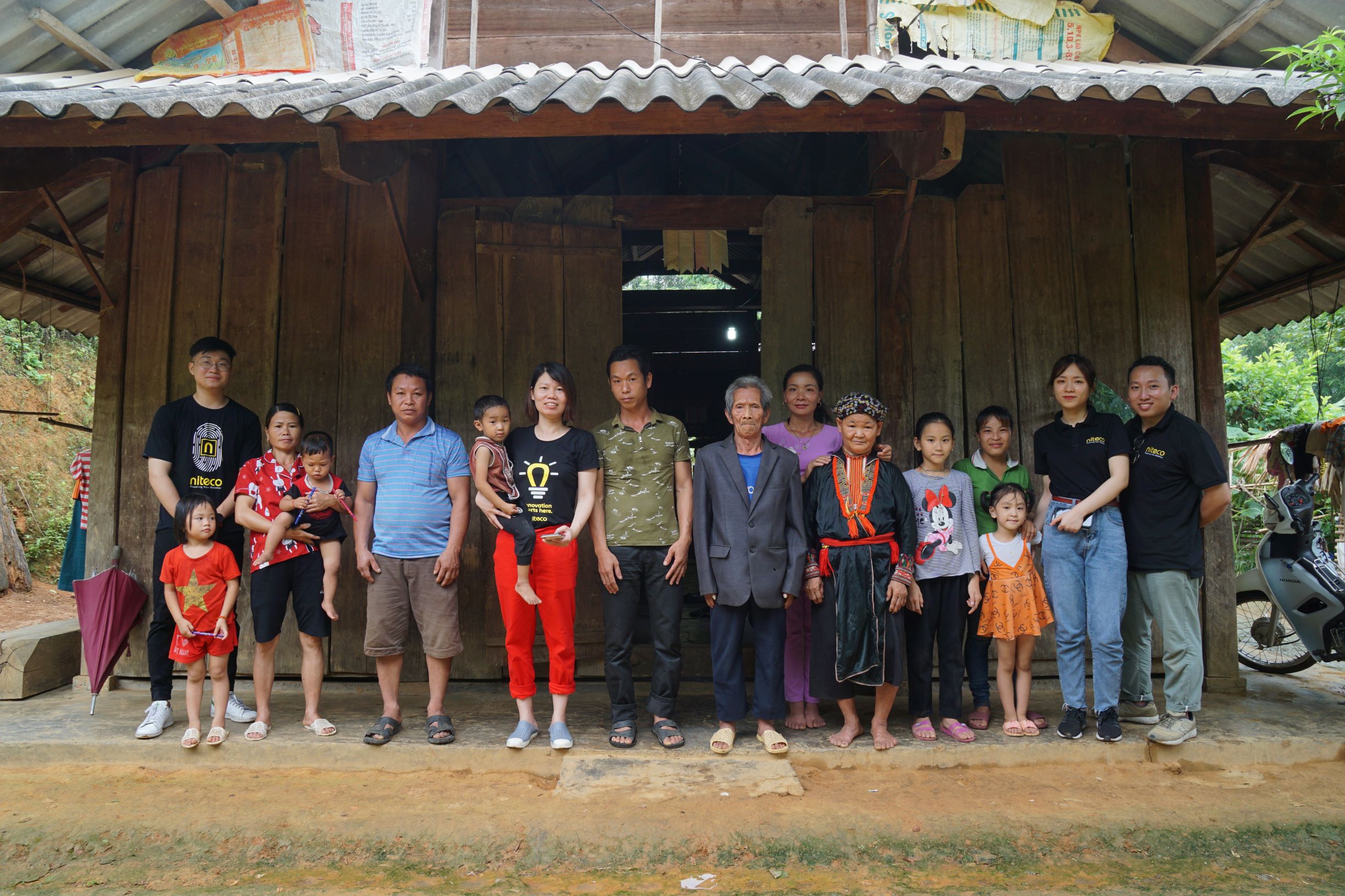 Community gathering of diverse families in traditional and casual clothing outside wooden house