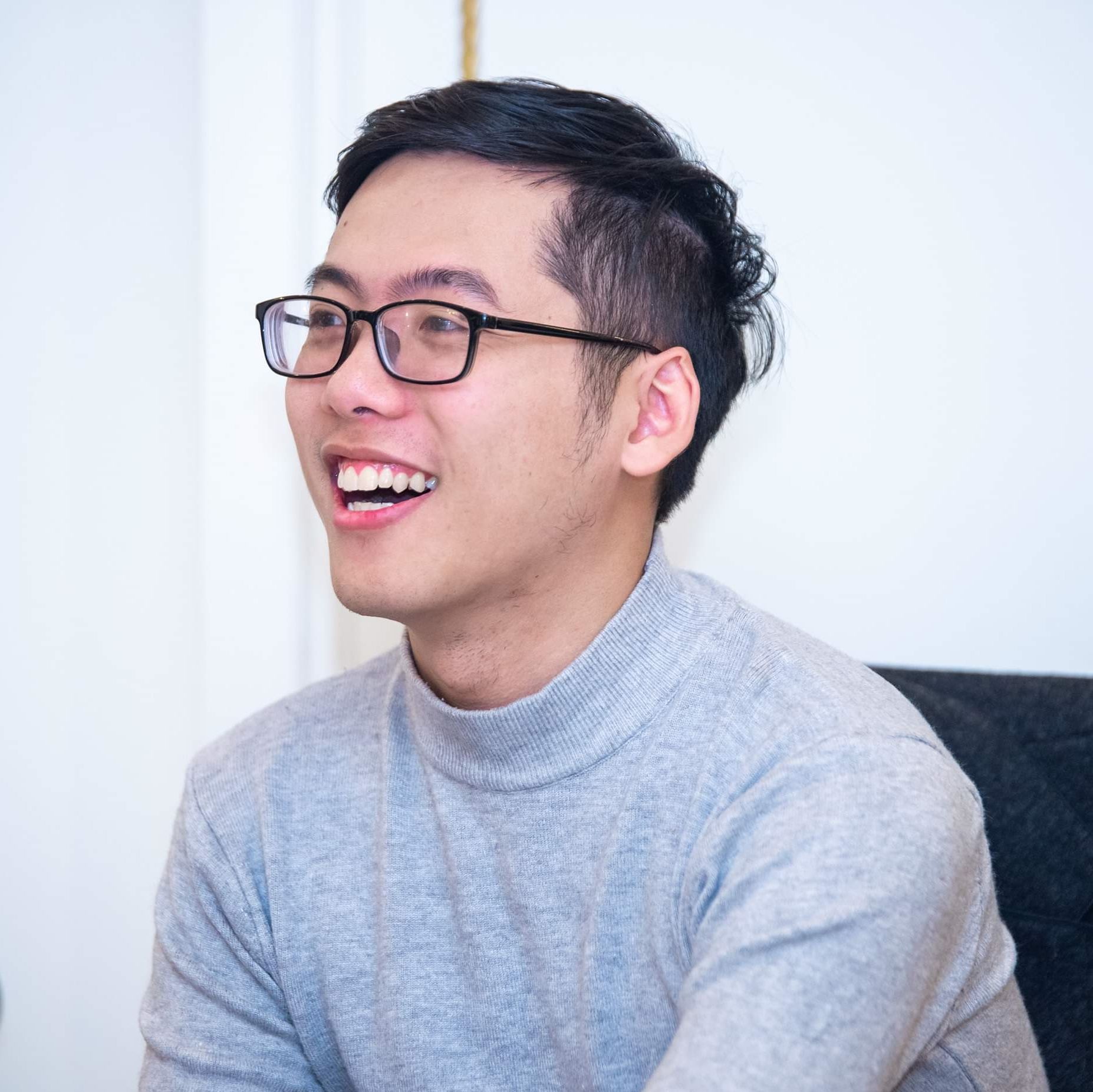 Smiling young man wearing glasses and gray sweater in a bright room