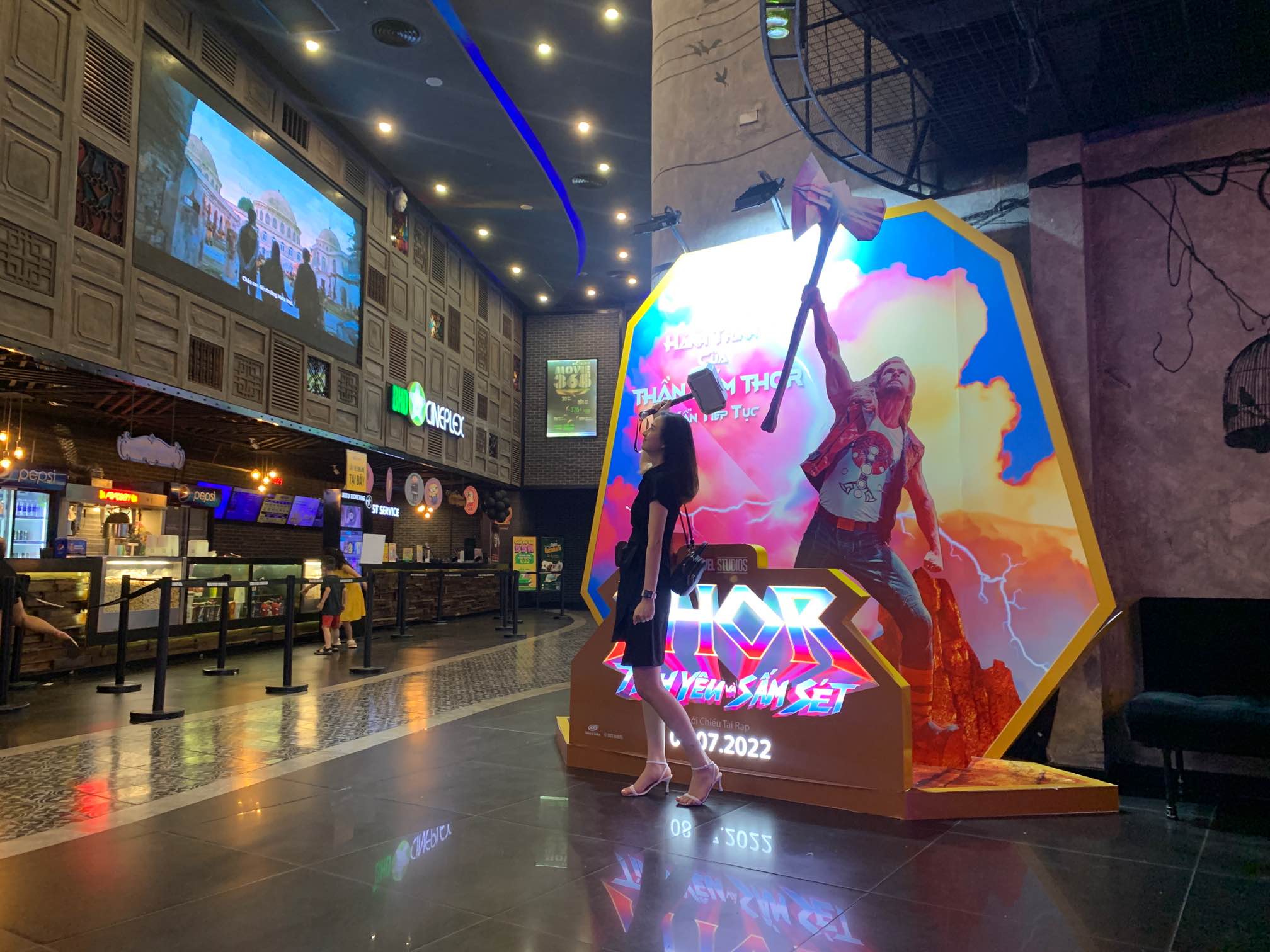 Thor movie display with a woman posing inside a modern cinema lobby