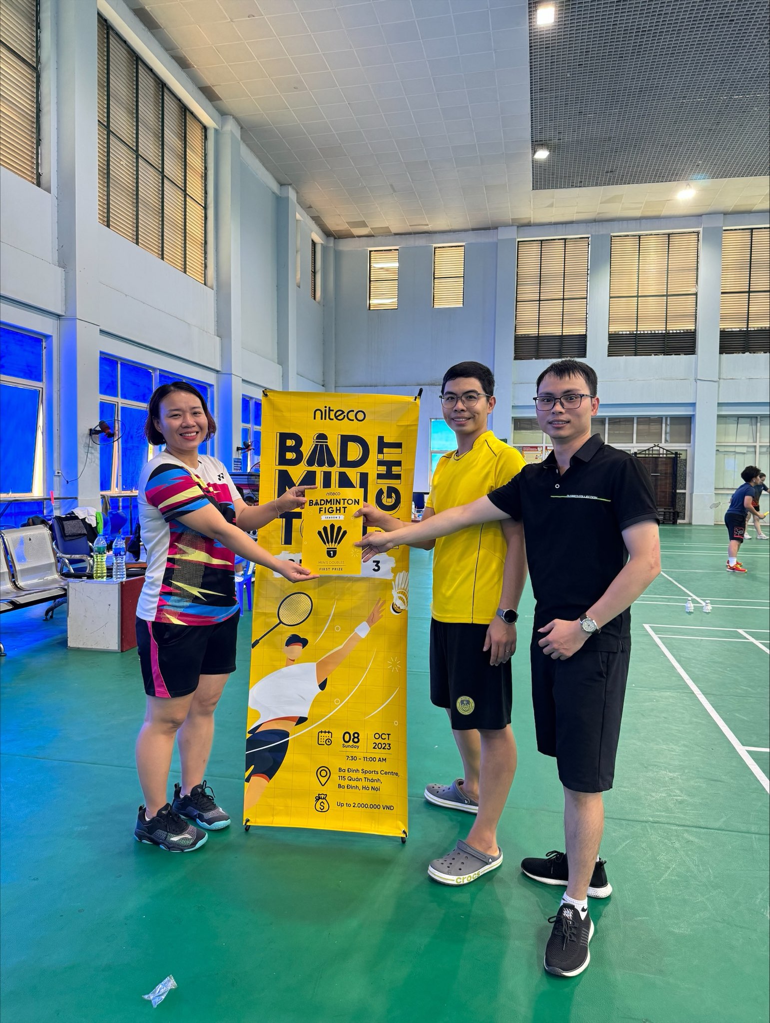 Three people holding a badminton fight first prize sign on indoor court