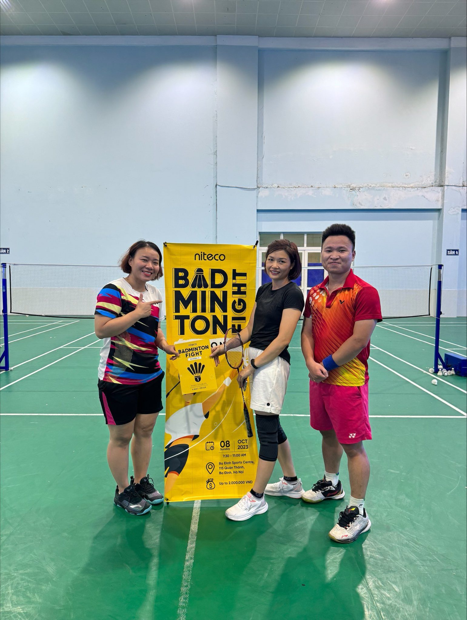 Three badminton players posing by the Niteco Badminton Fight event banner on court