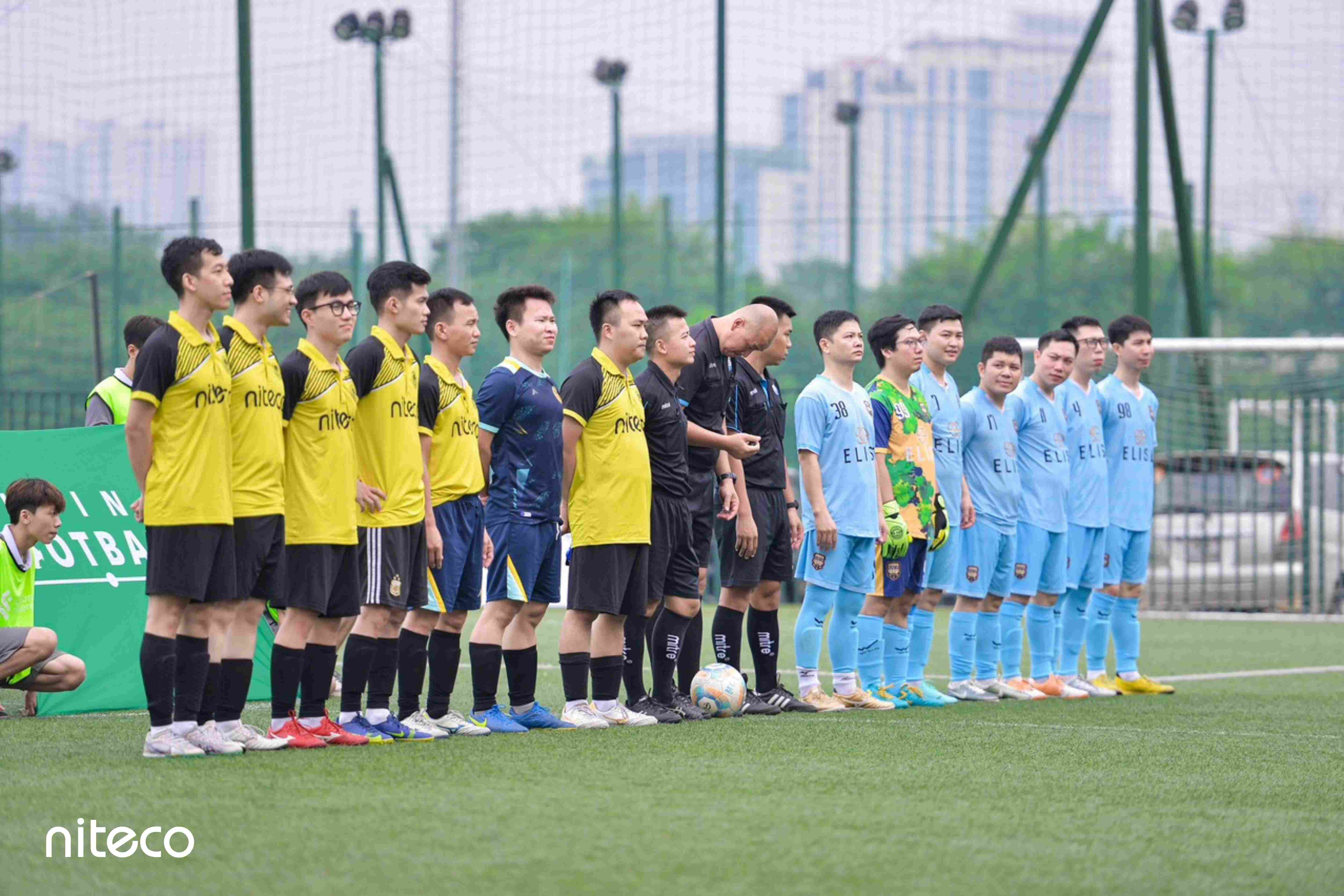 Teams in yellow niteco and blue elis jerseys lined up before soccer match