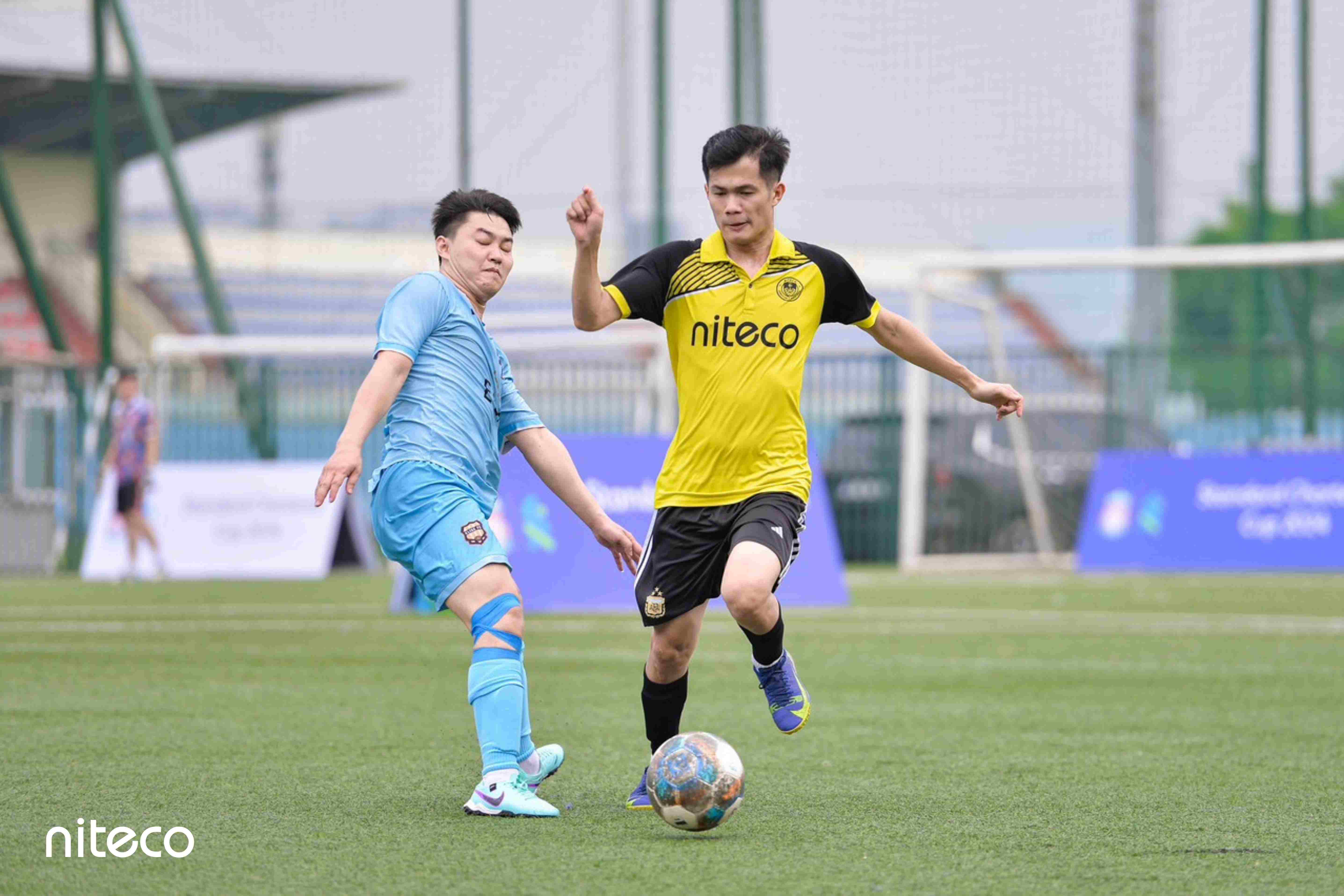Two soccer players compete for the ball during a Niteco football match on grass field