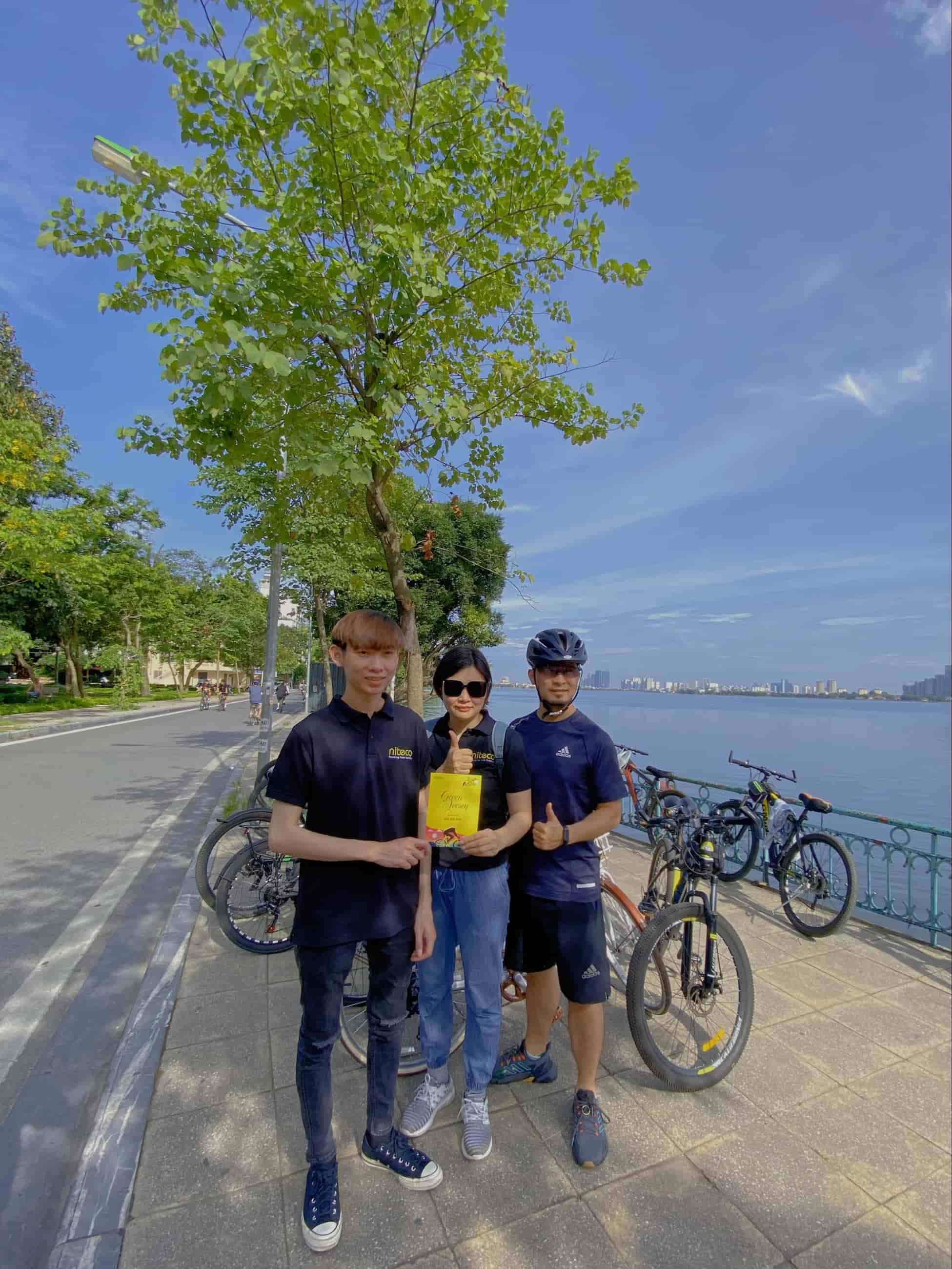 Three cyclists by the lake with bikes and holding a book outdoors