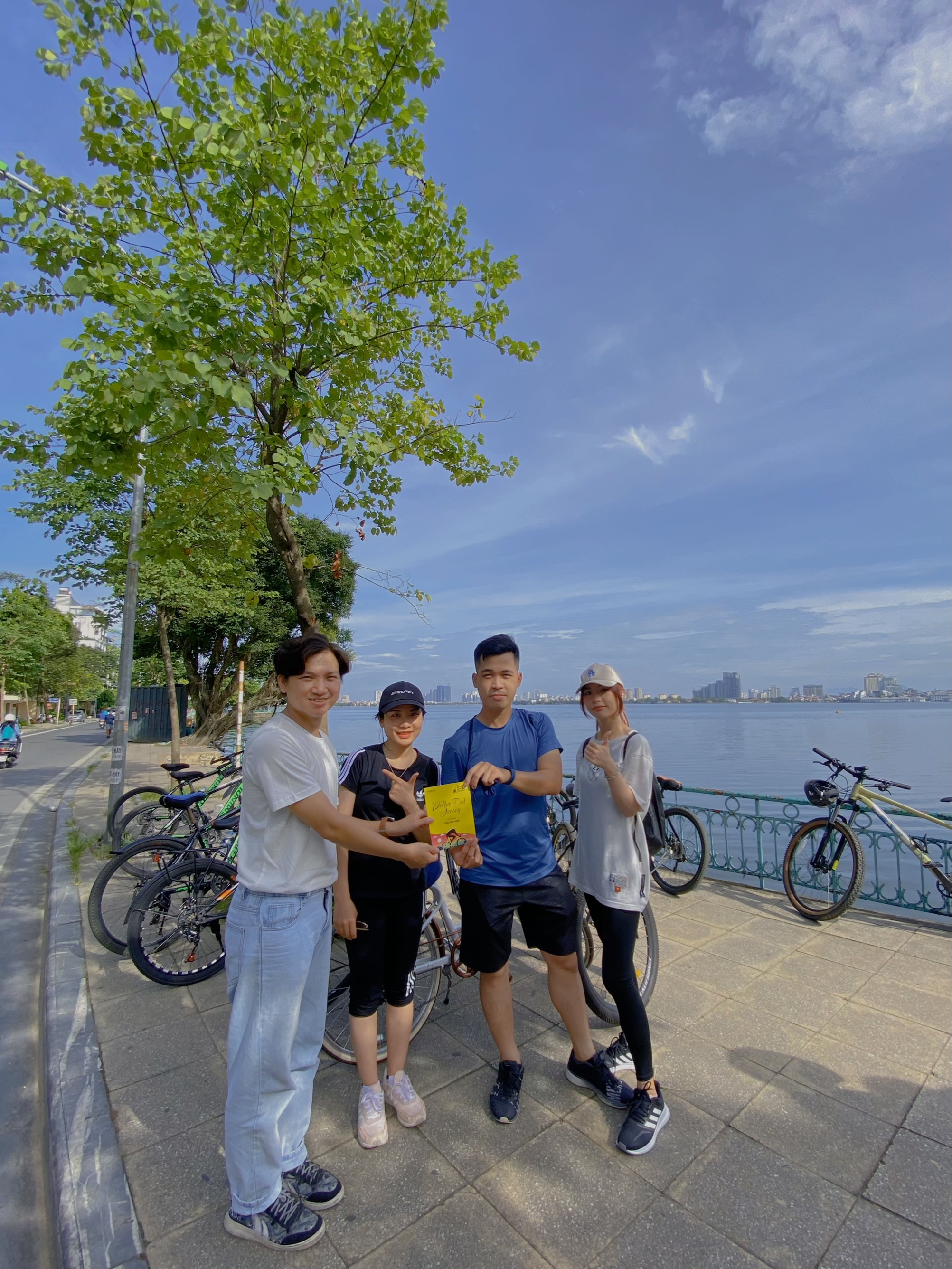 Four friends cycling by the lake sharing a Yellow Dot Jersey brochure outdoors