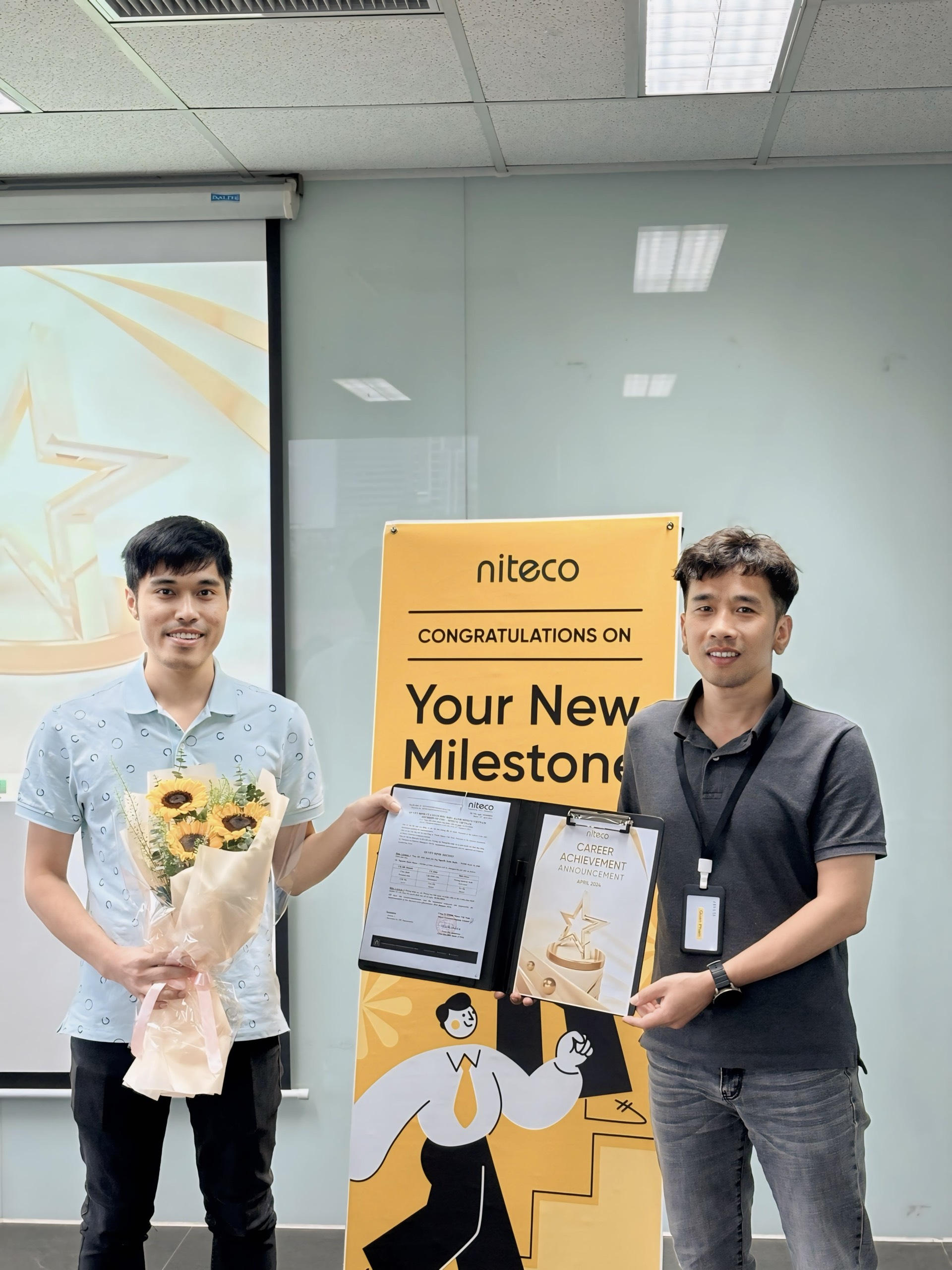 Two employees celebrating career achievement milestone with flowers and certificate