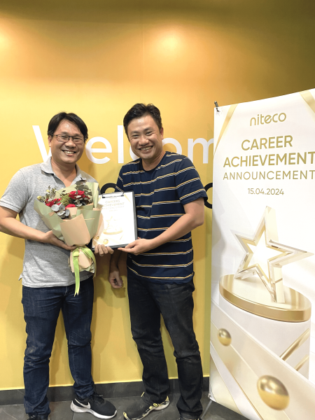 Two men celebrating career achievement award with flowers and certificate at Niteco event