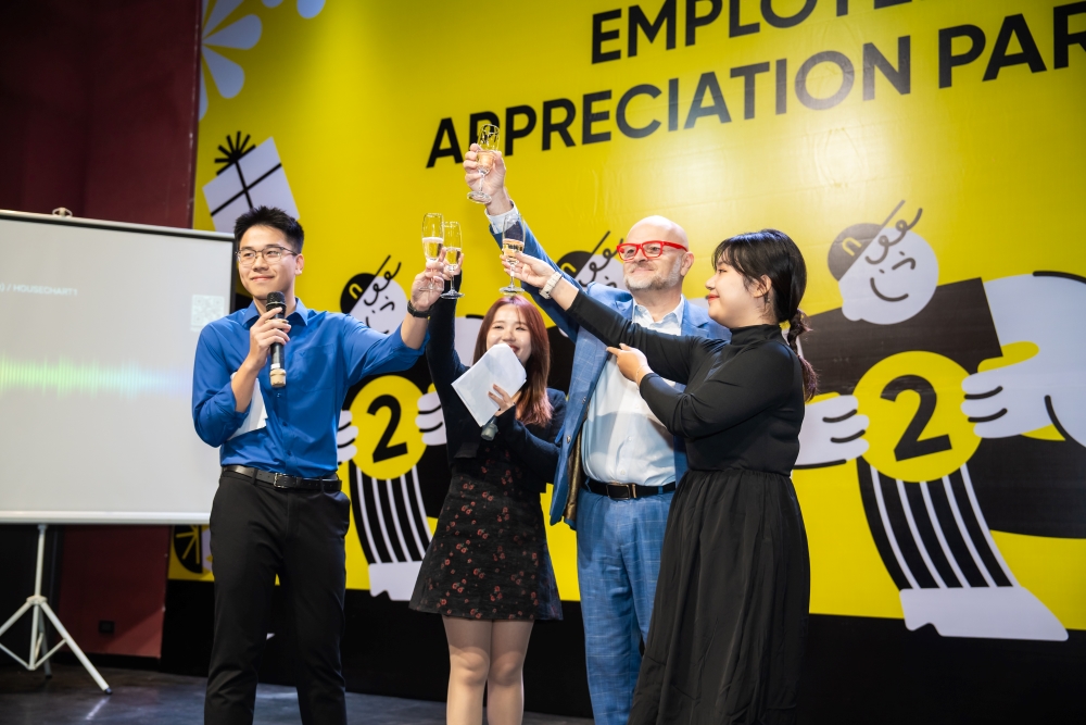 Four colleagues raise champagne glasses in front of a yellow Employee Appreciation Party backdrop