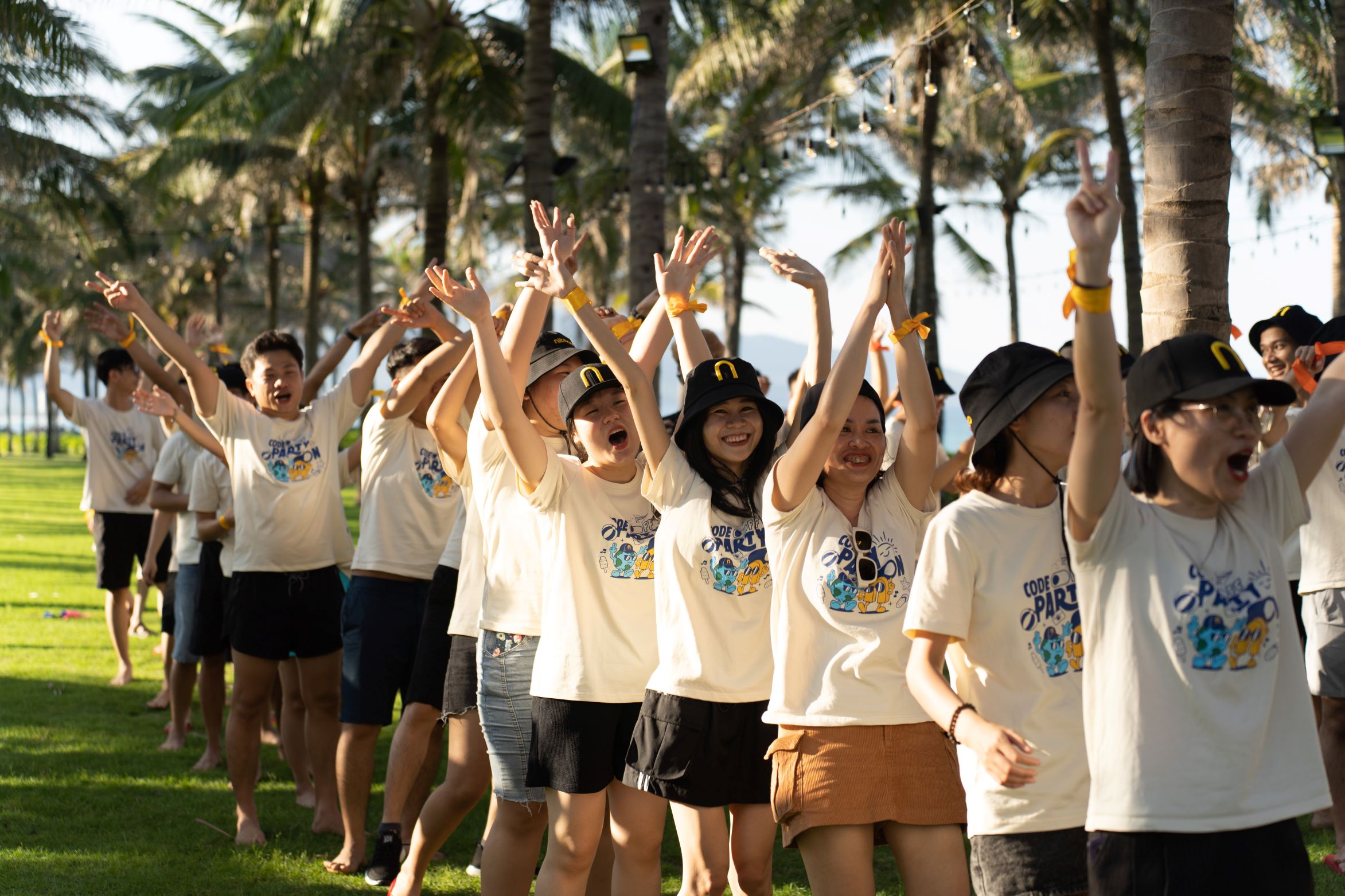 Team-building event participants raising hands and cheering outdoors under palm trees