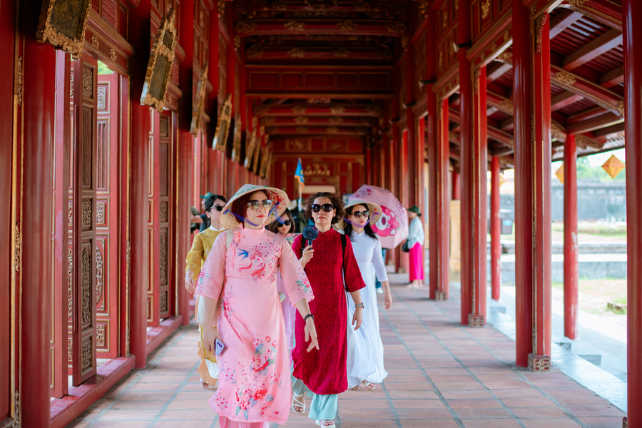 Vietnamese women in traditional Ao Dai walking through red ancient temple corridor
