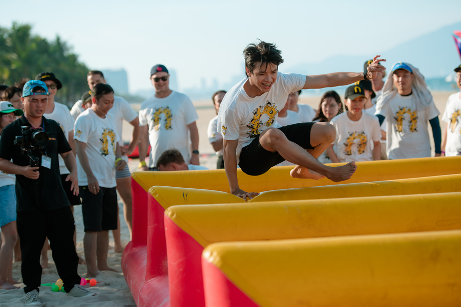 Young man jumping over inflatable obstacle in team building activity beach event