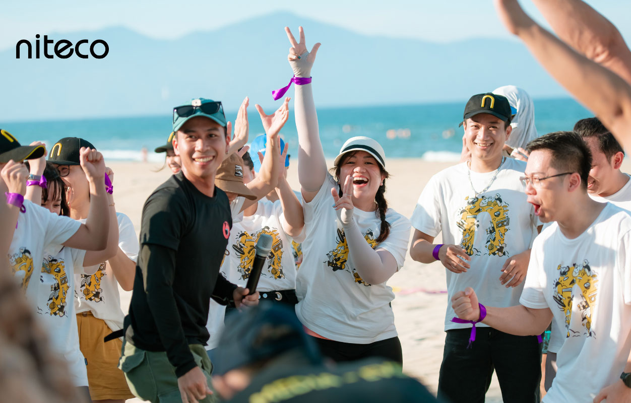 Niteco team celebrating together on the beach wearing branded white T-shirts