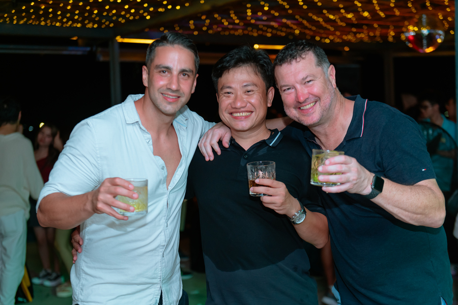 Three men enjoying drinks and smiling under string lights at party