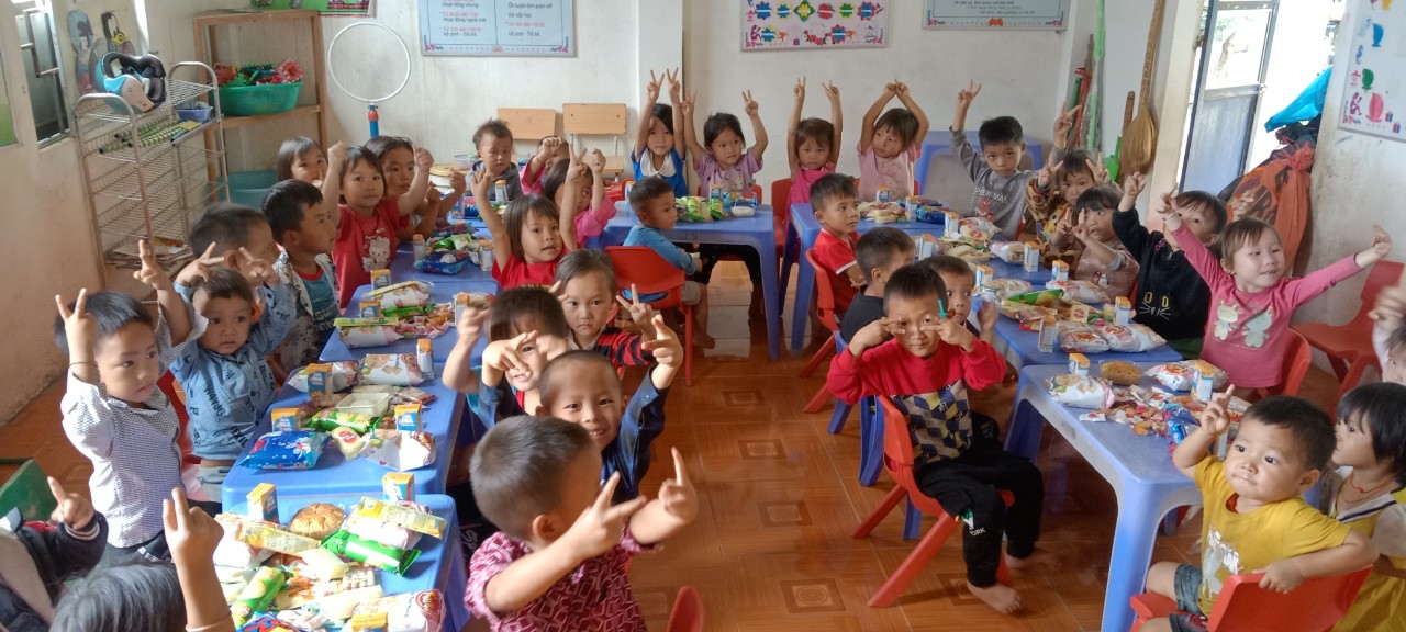 Kindergarten children enjoying snack time raising hands in classroom