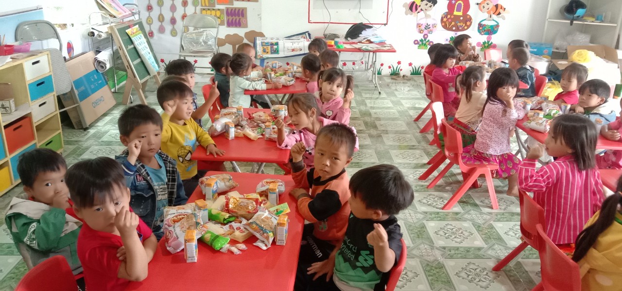 Preschool children eating snacks together at colorful tables in classroom