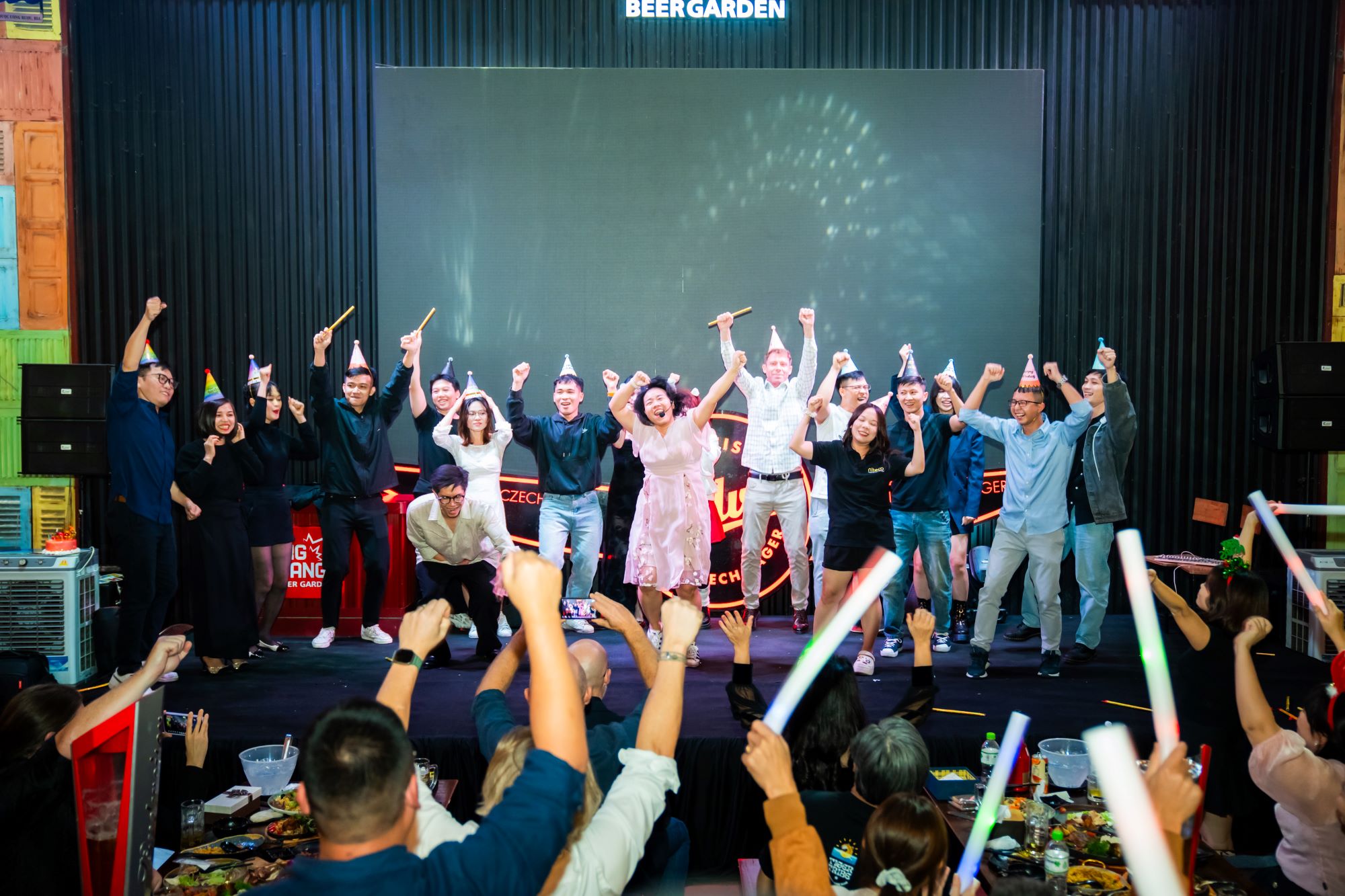 Group celebration at beer garden party with raised hands and party hats