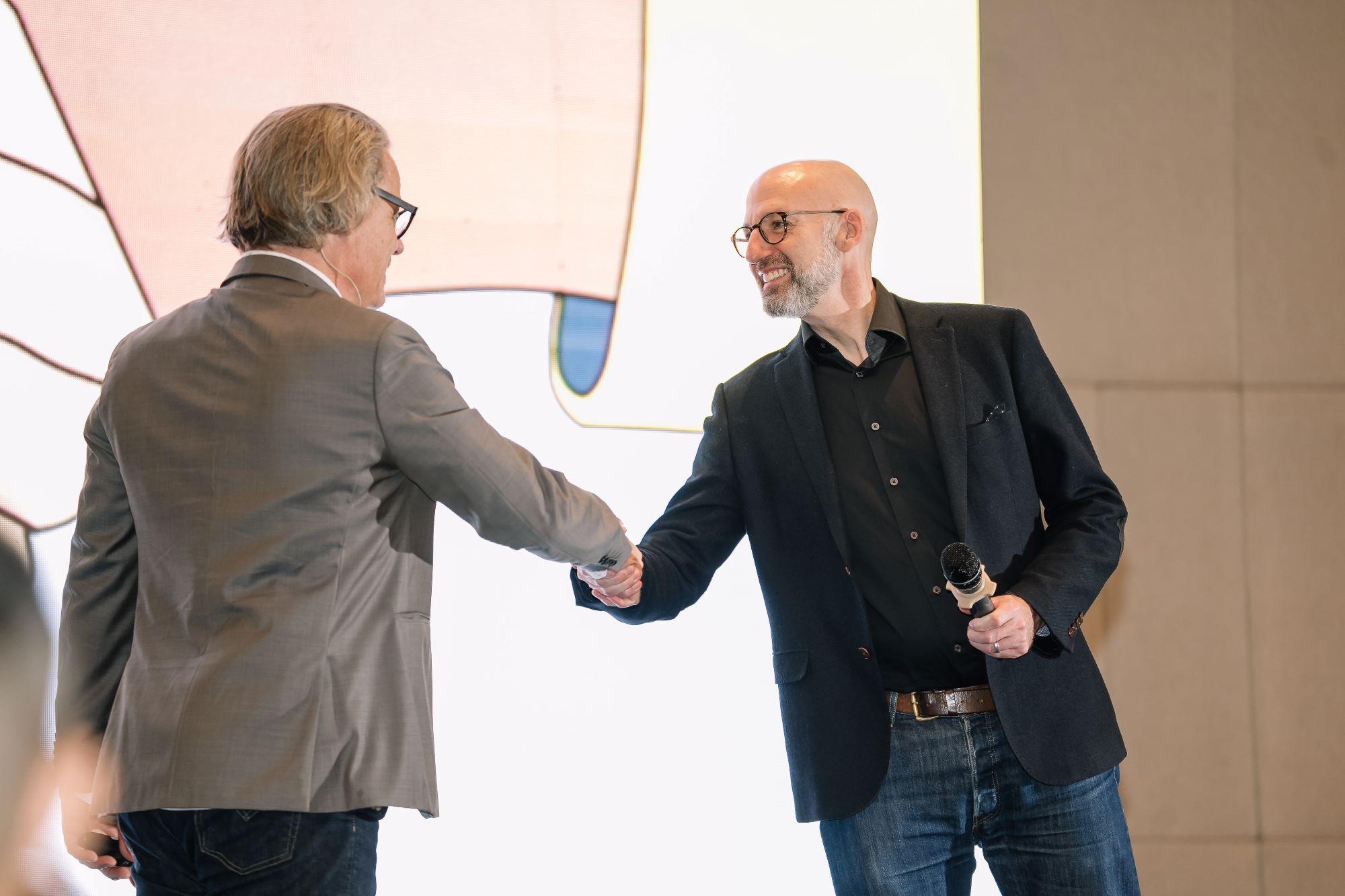 Two businessmen shaking hands during a conference presentation with microphone