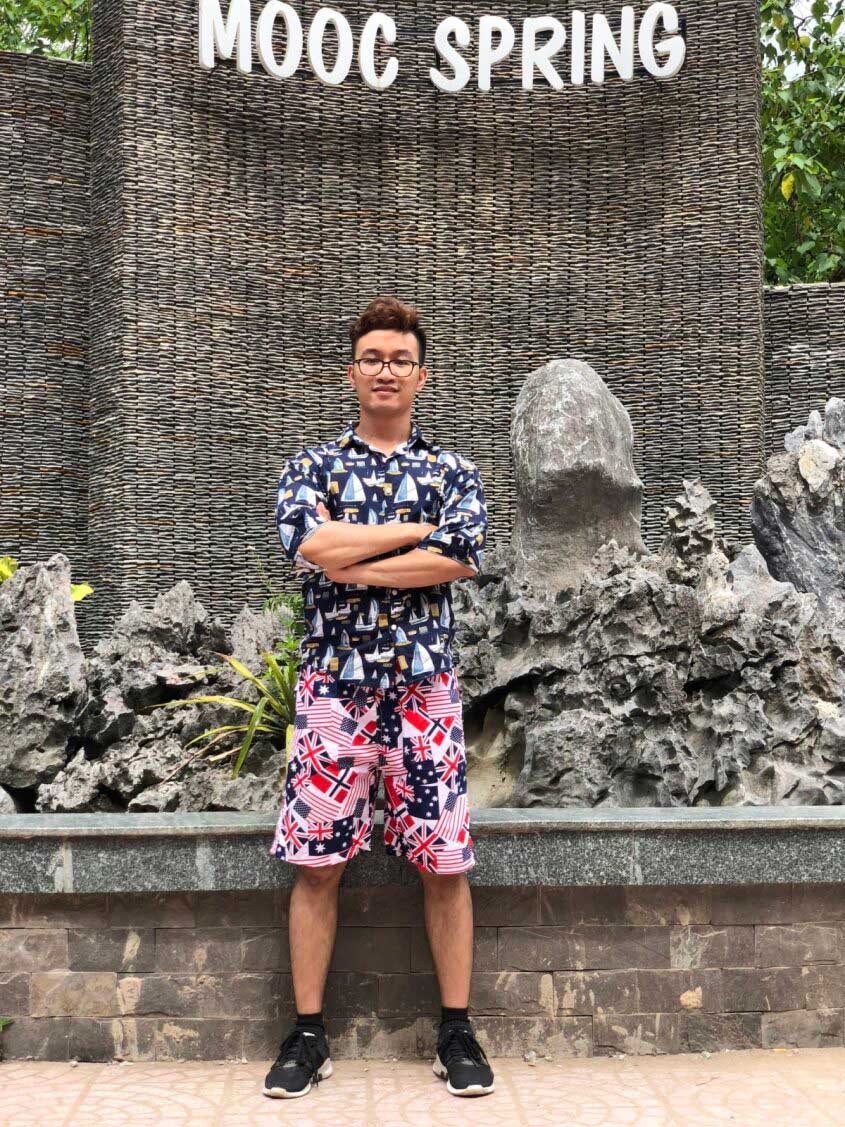 Young man standing confidently in front of MOOC Spring sign and rock wall