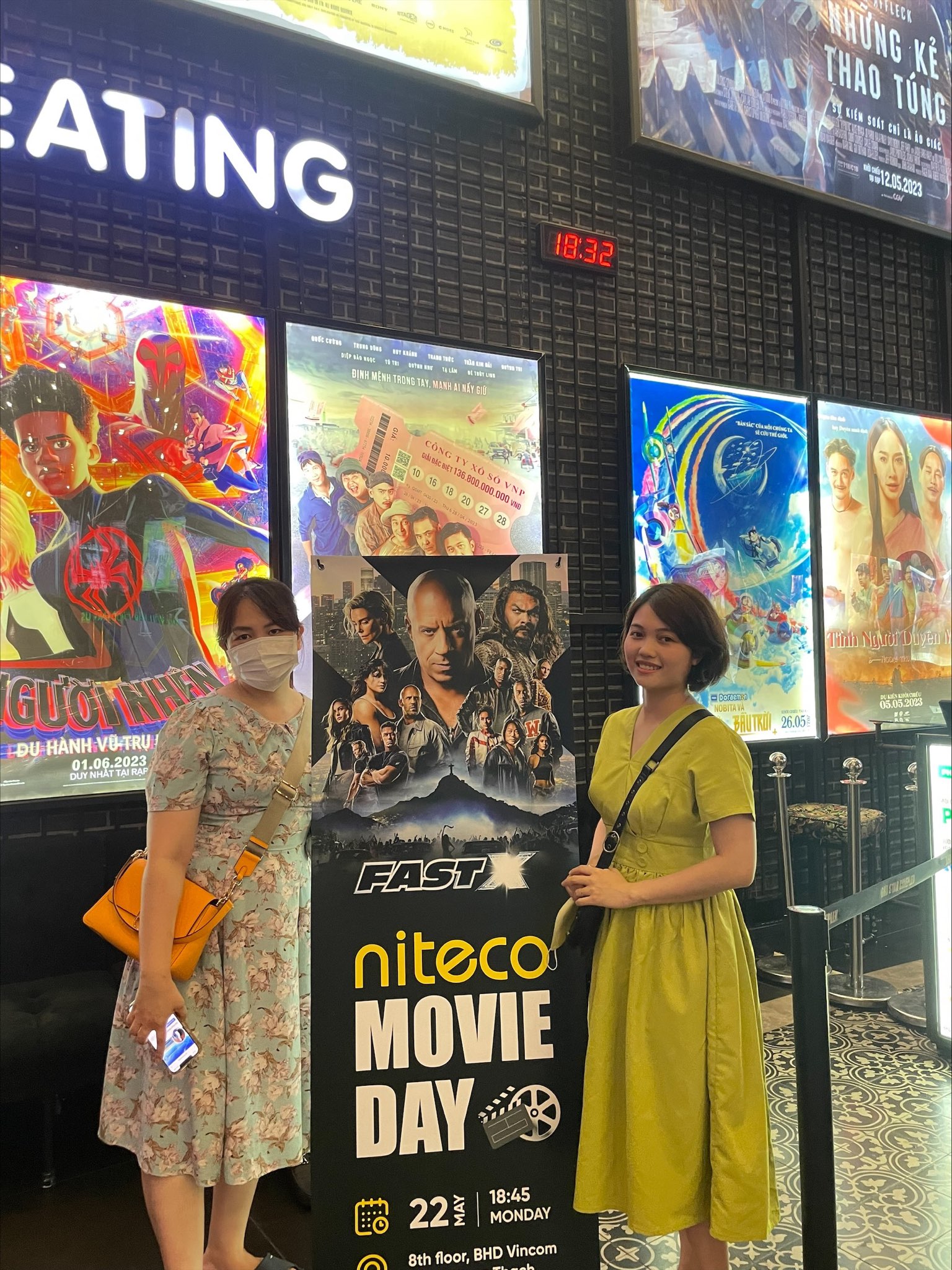 Two women posing beside Fast X poster at Niteco Movie Day event in cinema lobby