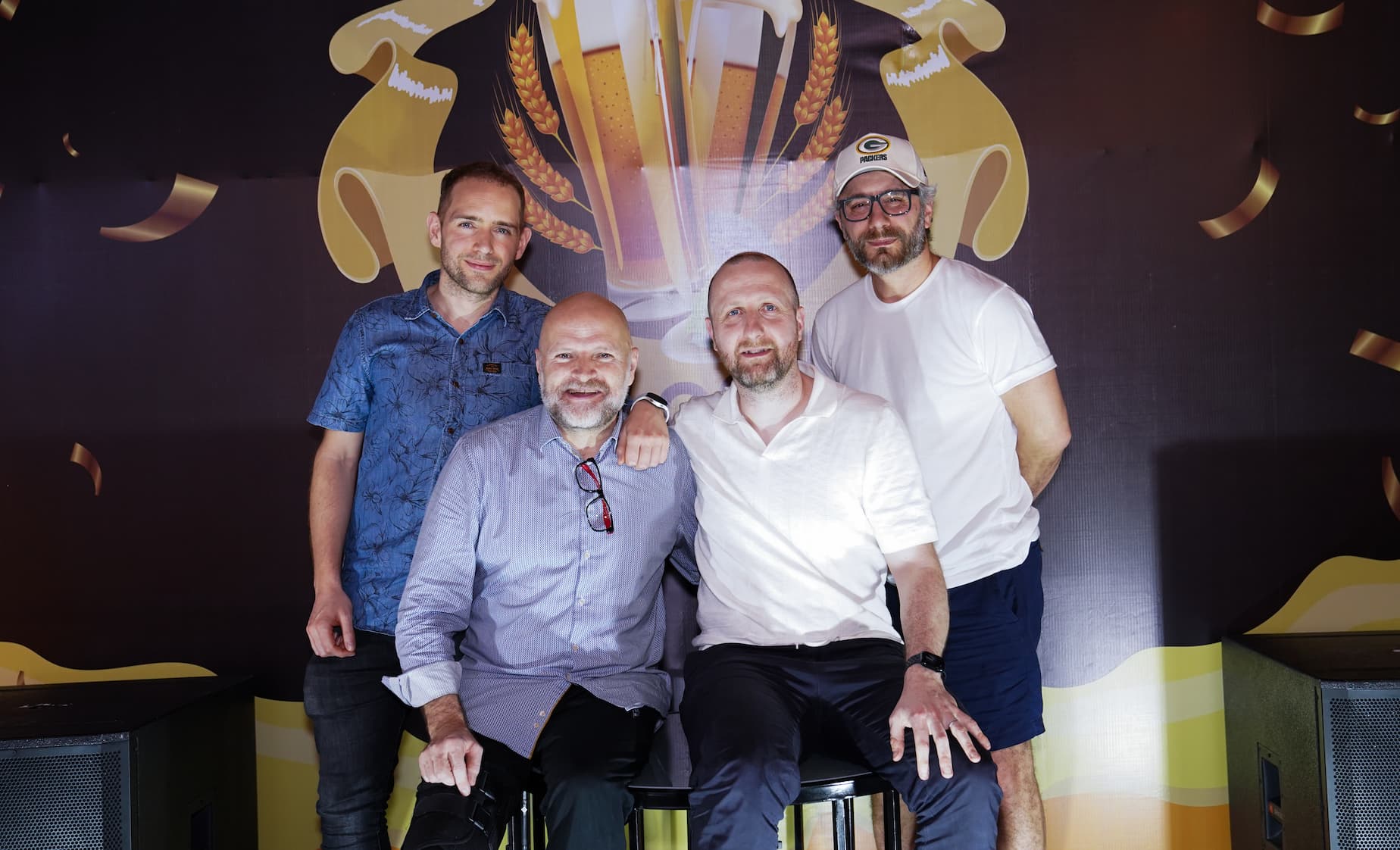Group of four men enjoying Beer Festival with decorated backdrop and trophies
