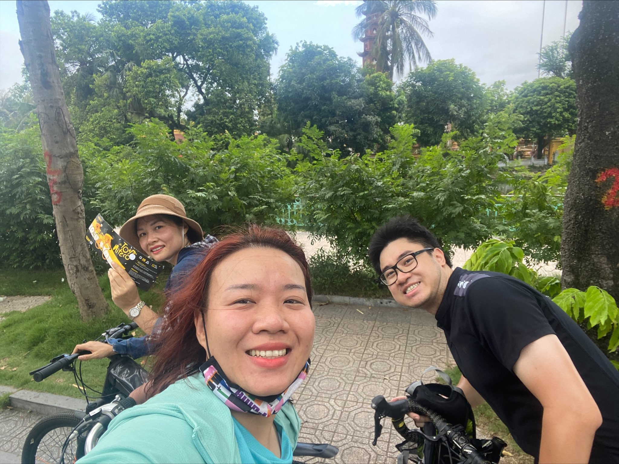 Three friends biking outdoors smiling with lush greenery and trees behind them