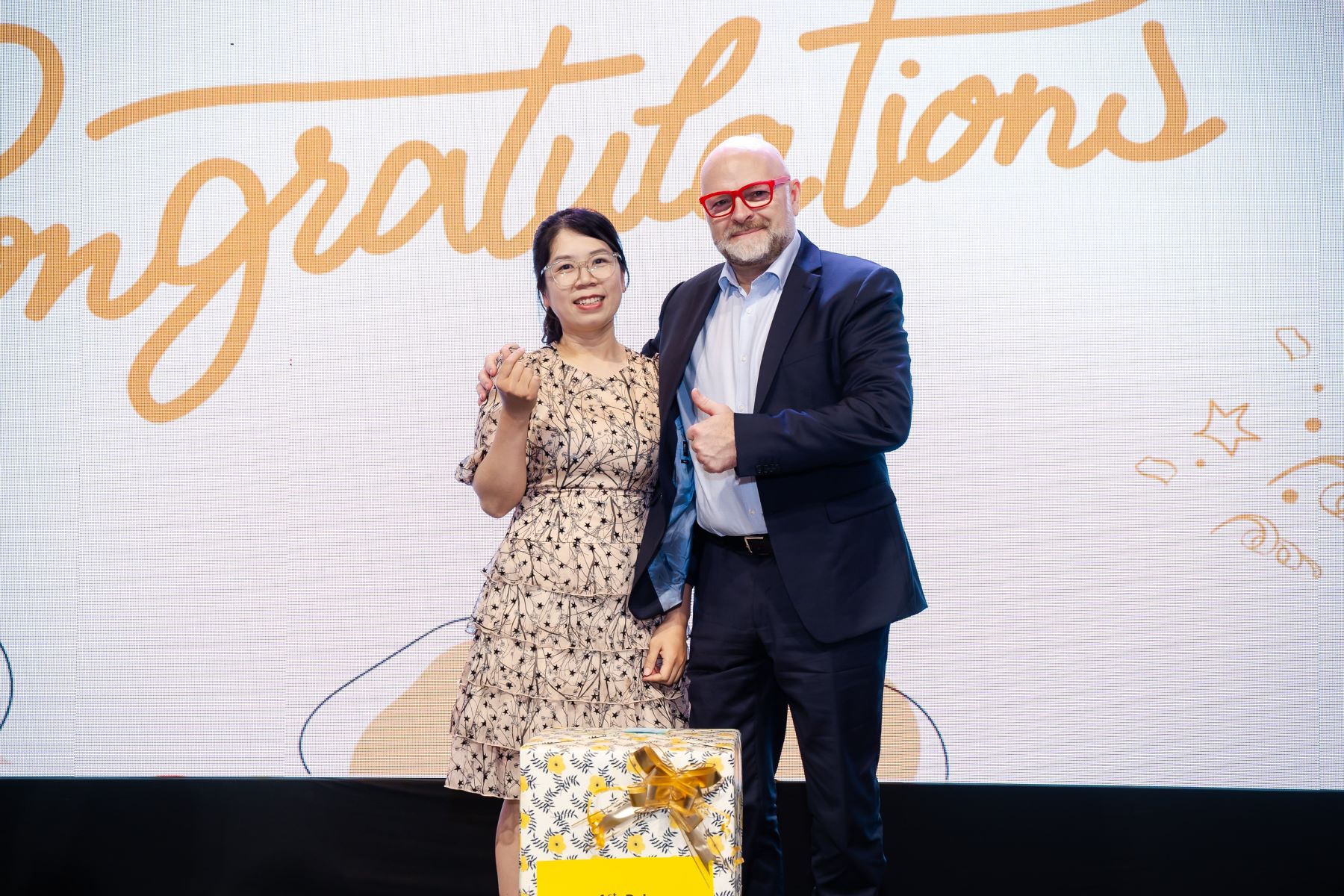 Two colleagues celebrating success with gift and congratulations background