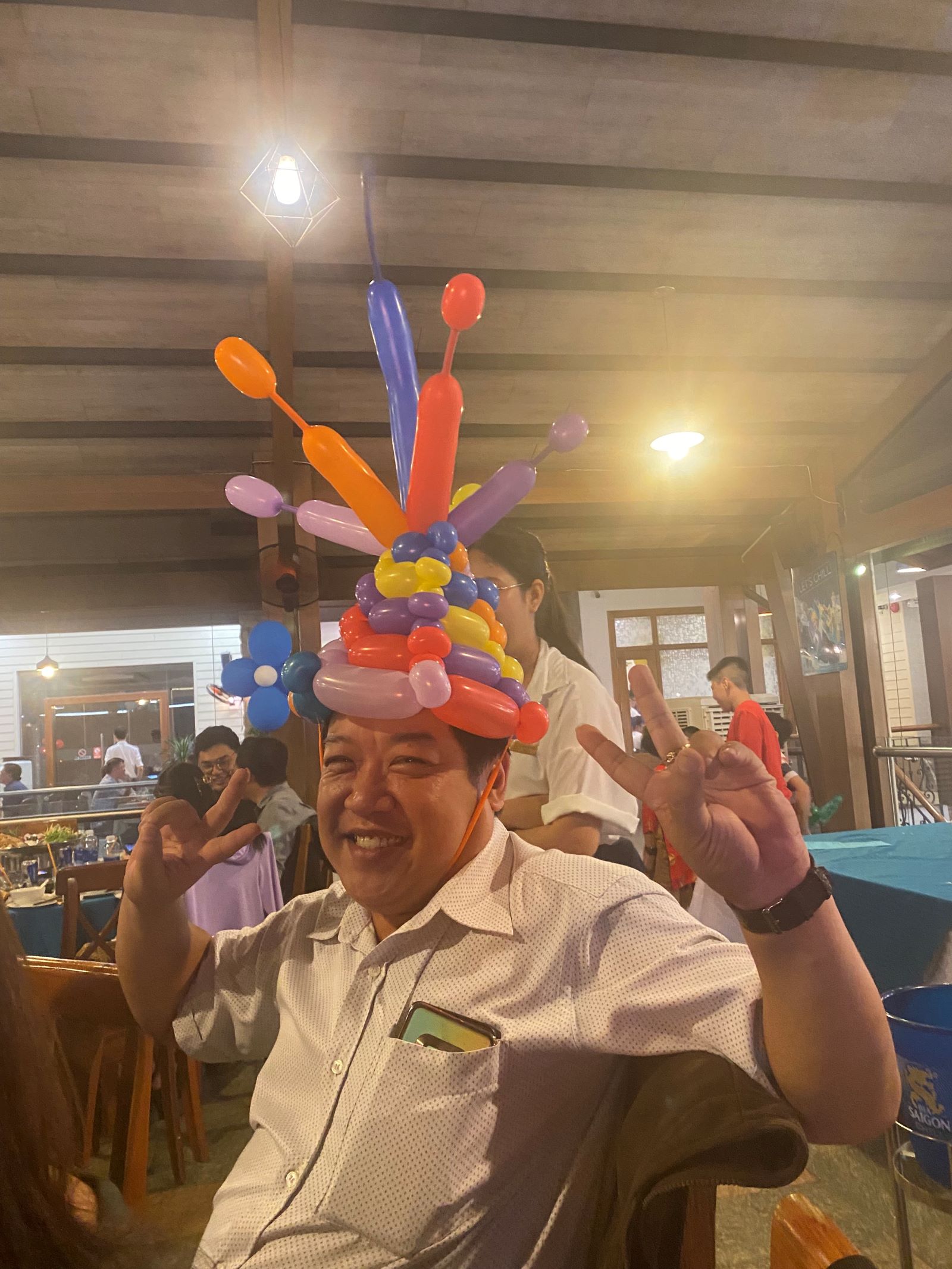 Man celebrating party with colorful balloon hat and showing peace signs