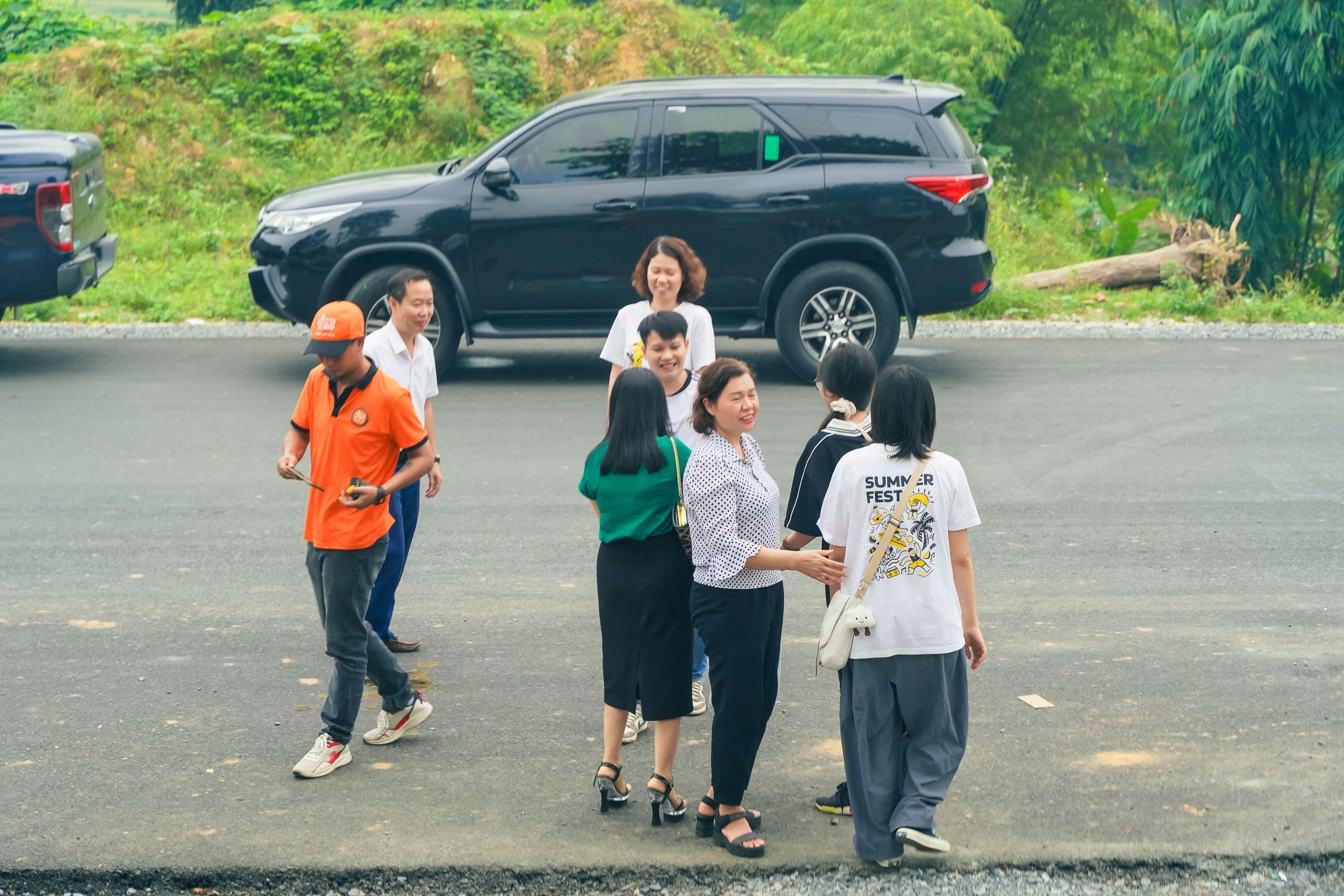Group of people socializing near parked black SUV in outdoor setting