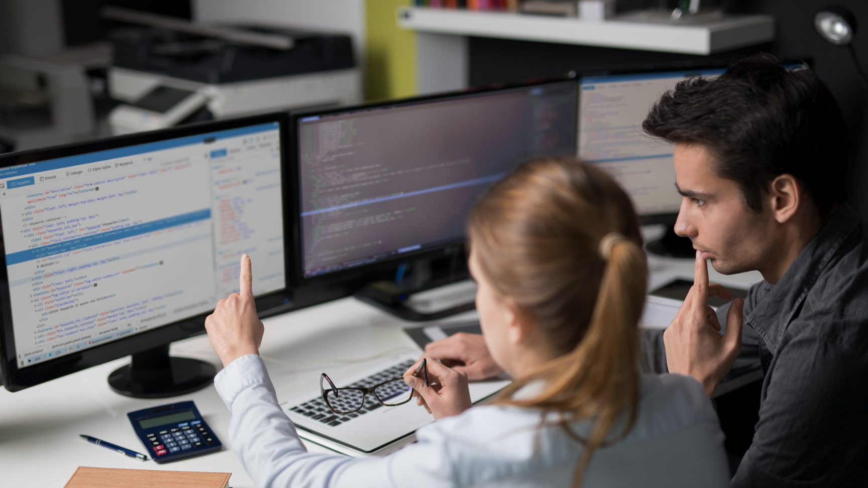 Two software developers collaborating on coding and debugging with multiple monitors