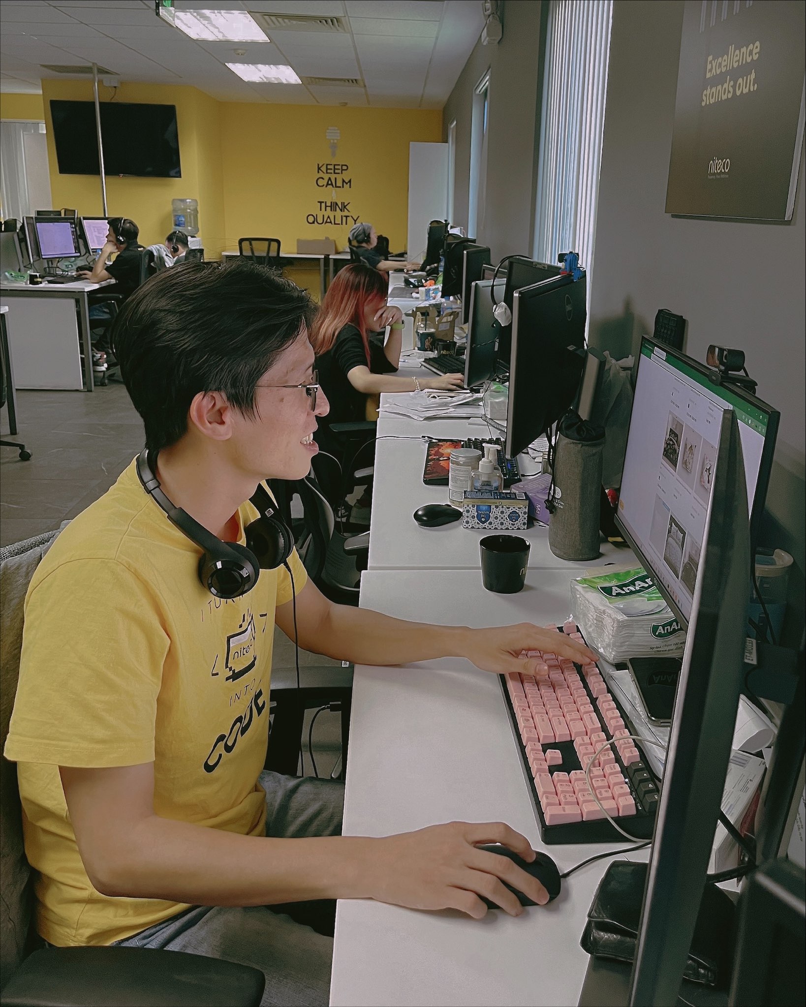 Young developer coding on a computer with a pink keyboard in a busy office