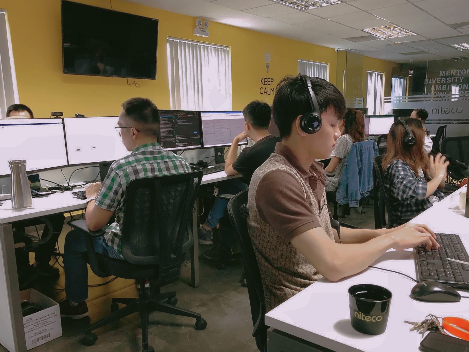 Software developers working in an open office with multiple monitors and headsets