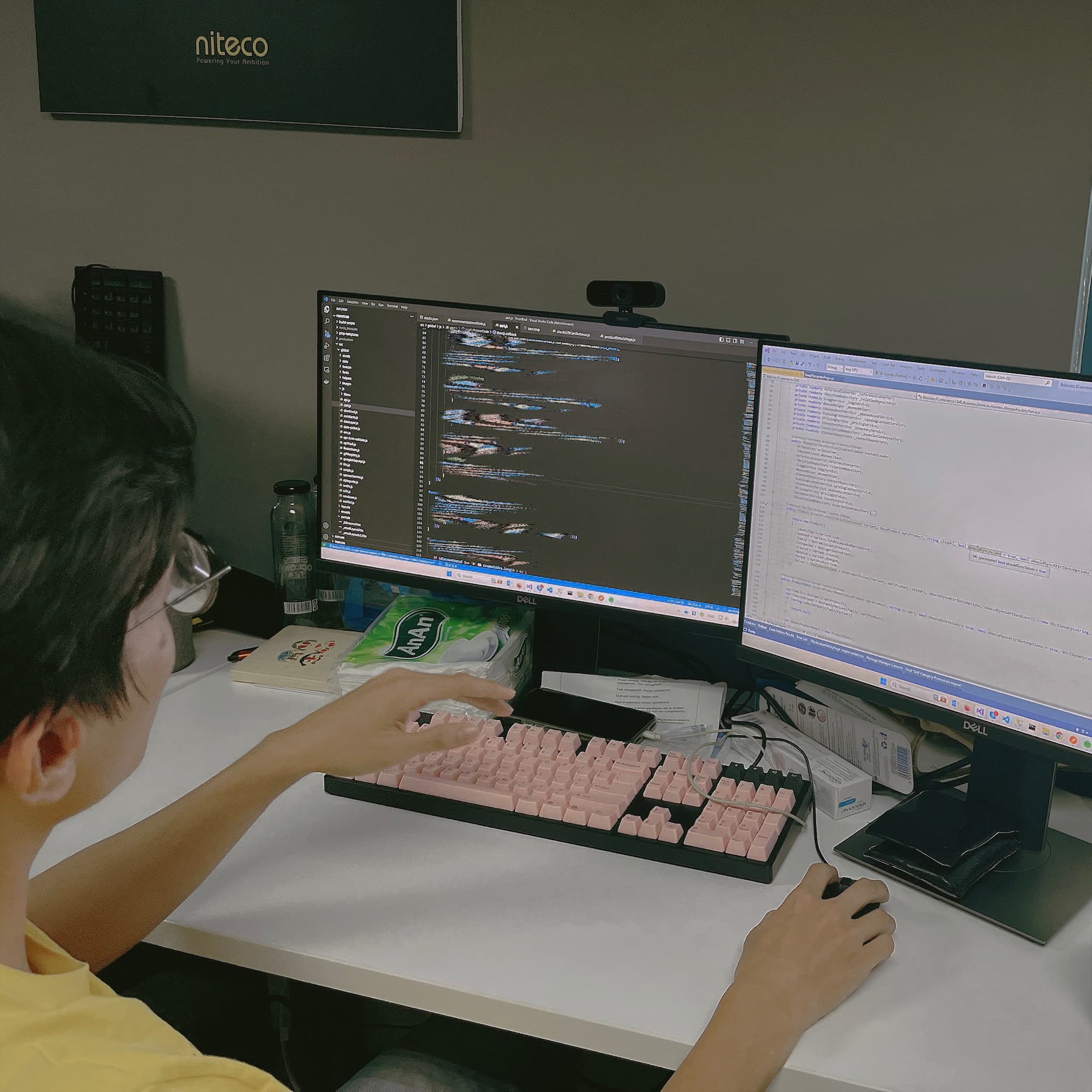 Developer working on coding with dual monitors and pink keyboard at desk