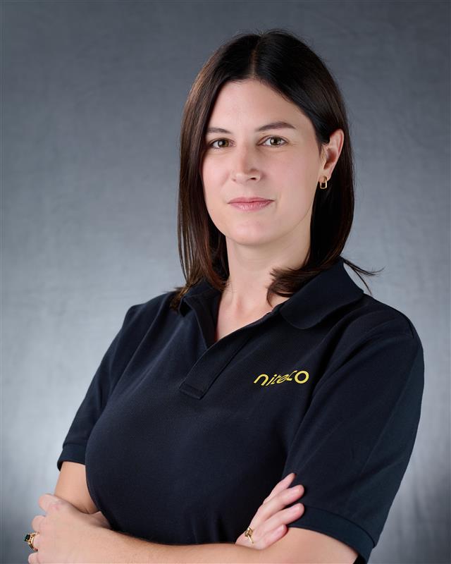 Woman with dark hair wearing a black shirt with crossed arms on a gray background.