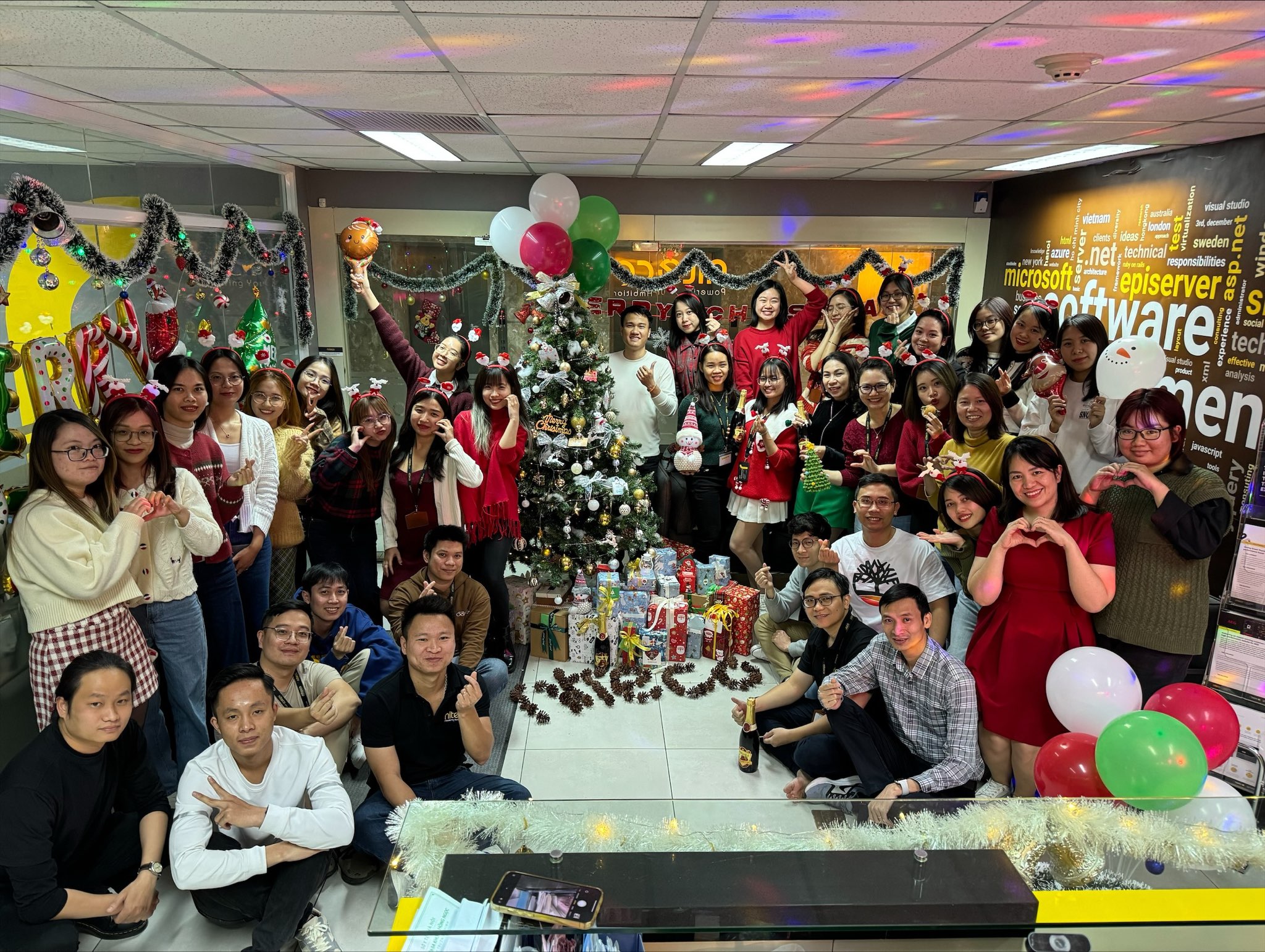 Office team celebrating Christmas with decorated tree, gifts, and festive balloons